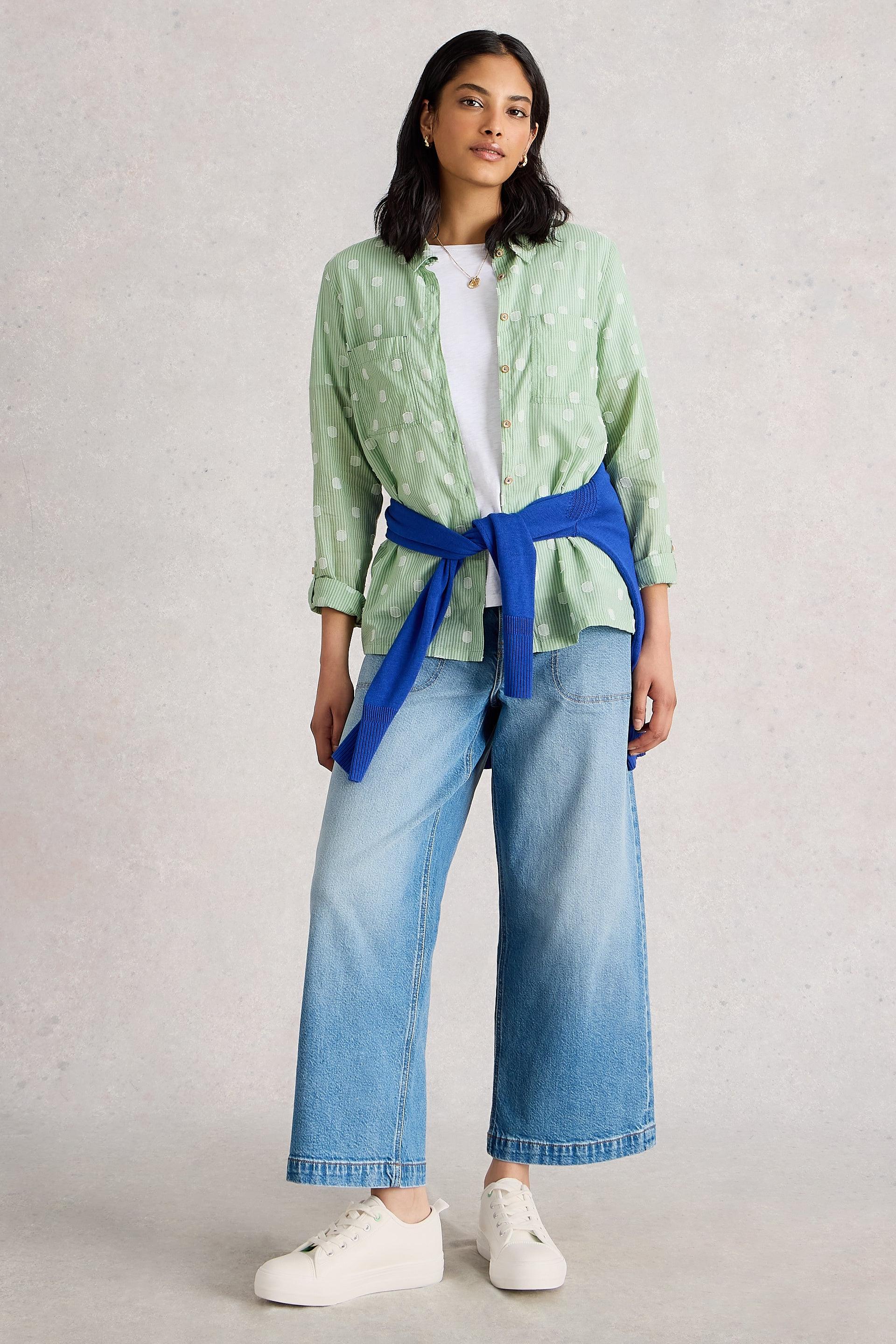 Woman standing wearing a green striped White Stuff shirt, blue wide-leg jeans, and white sneakers.