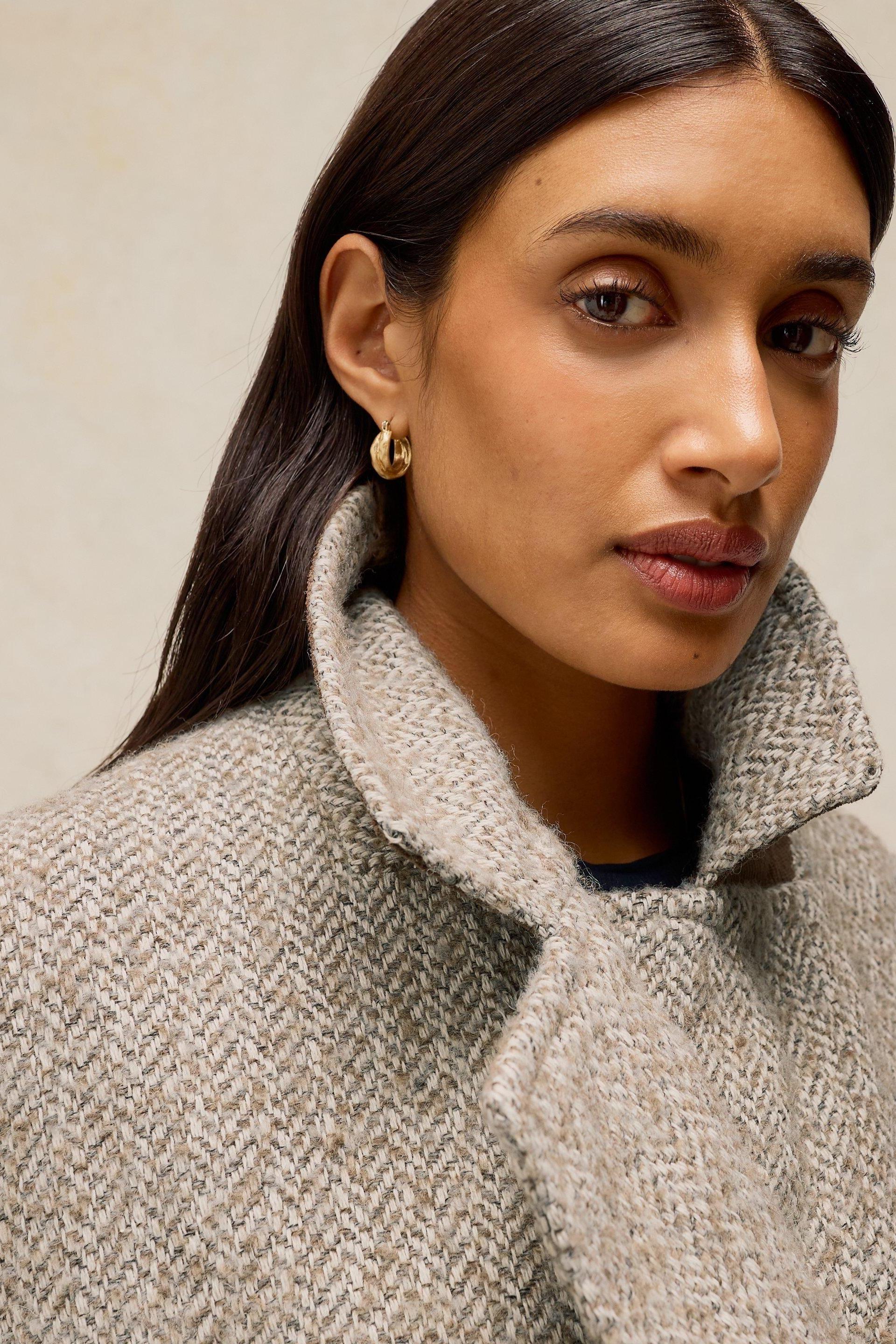 A woman wearing a textured natural colour wool coat with a high collar.