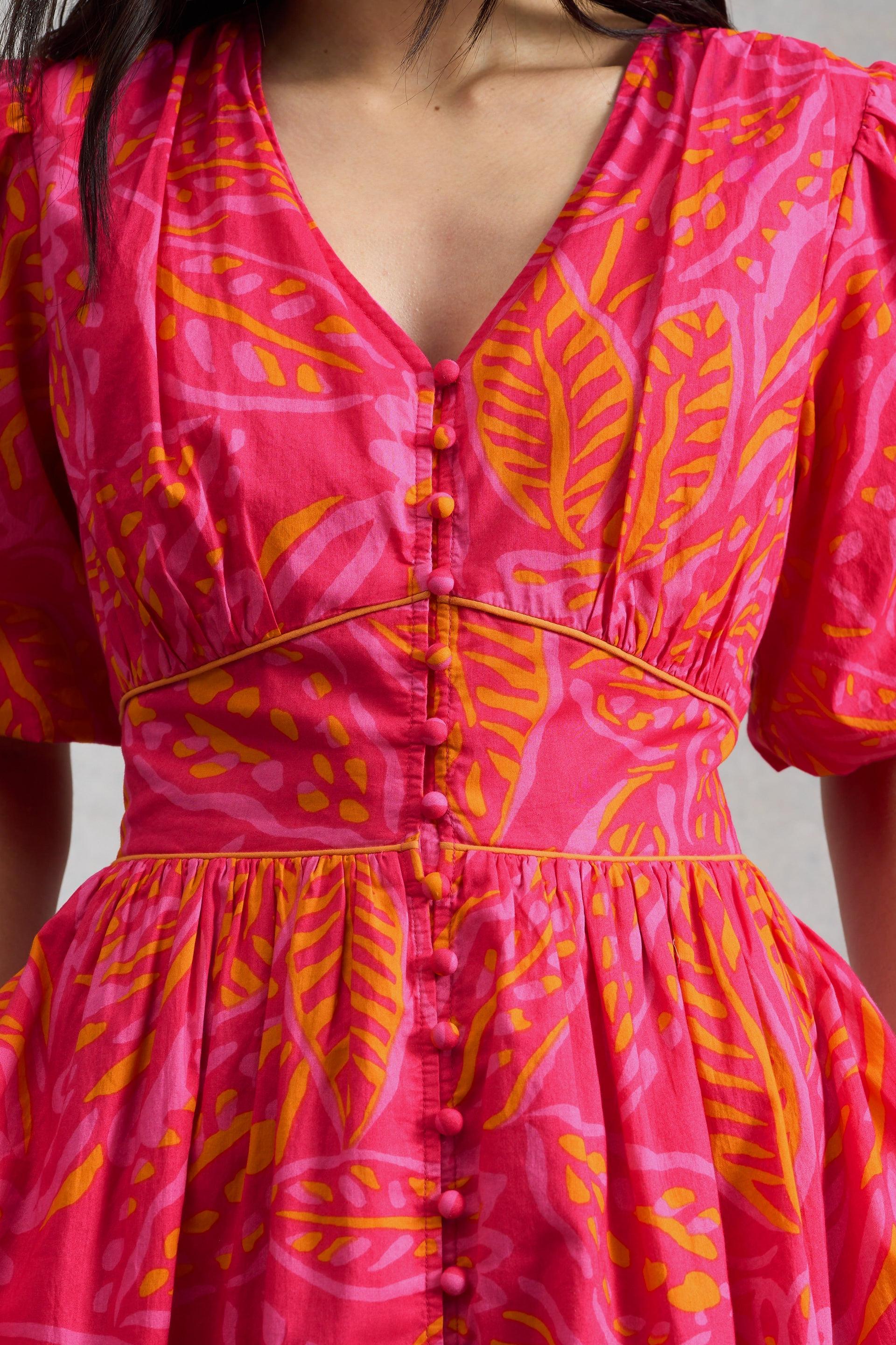 A woman wearing a vibrant pink and orange floral print organic cotton midi dress with button details.