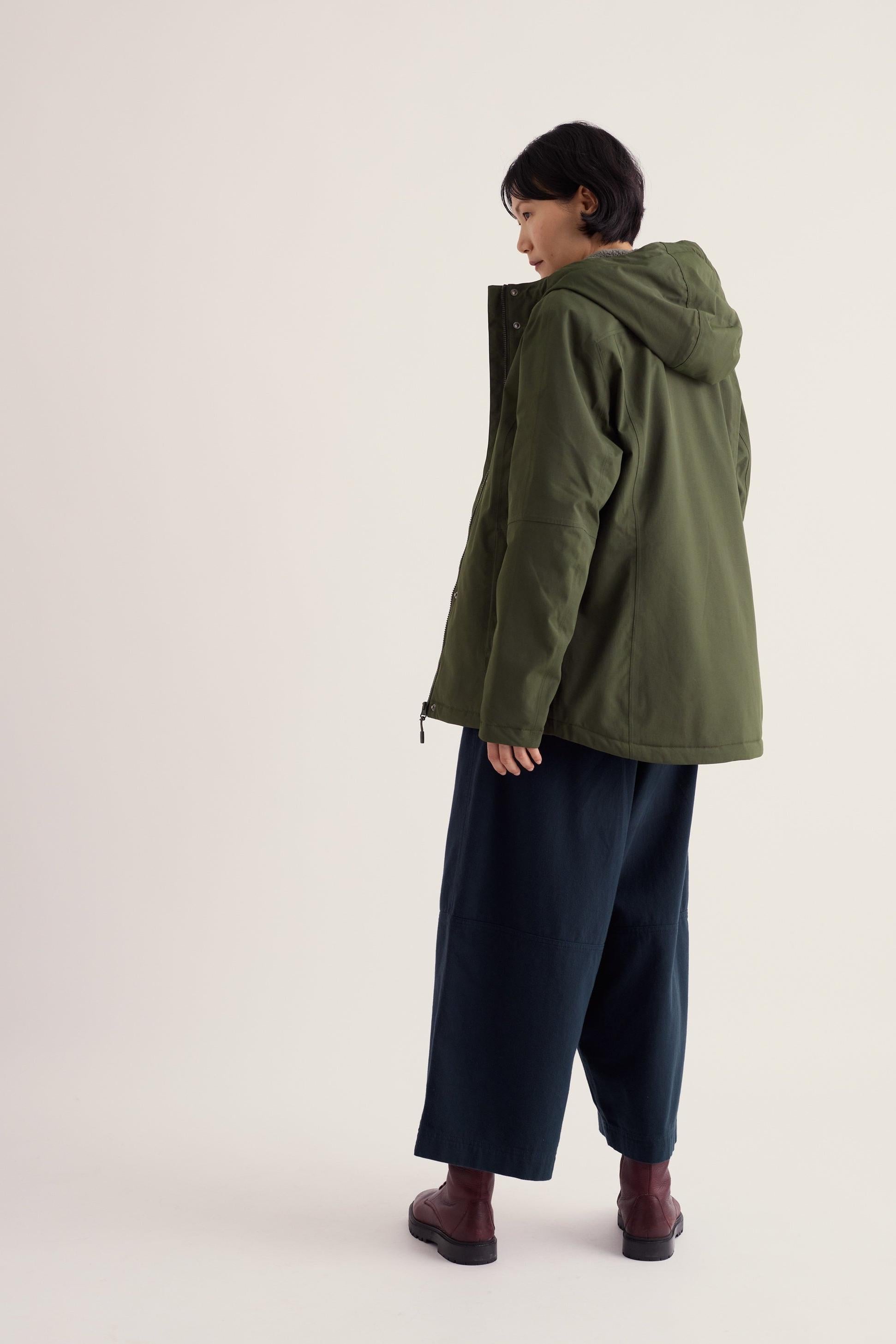 Woman wearing a woodland green Seasalt Cornwall waterproof jacket against a white background.