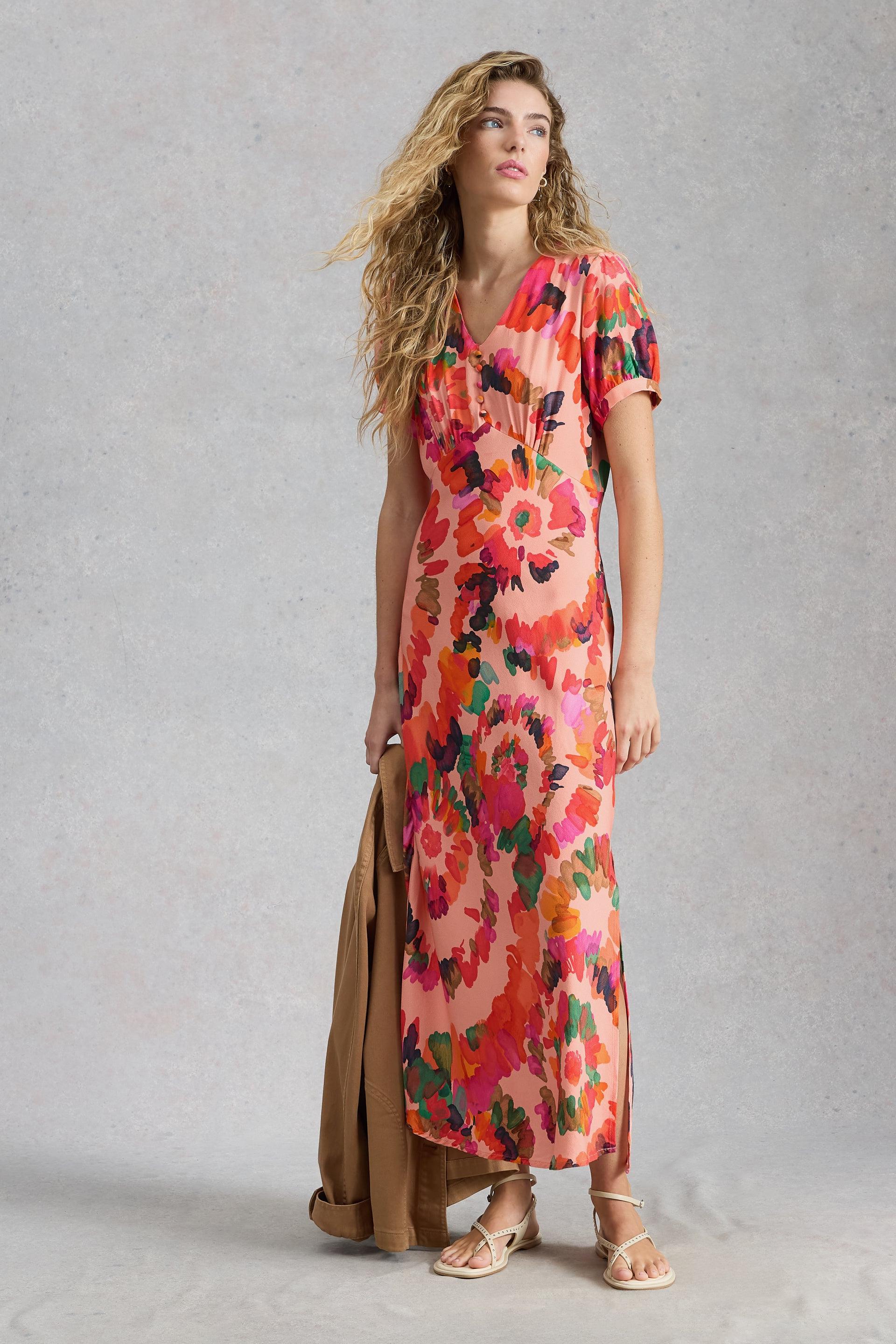 A woman posing in a vibrant floral occasion dress, embodying sustainable fashion style.