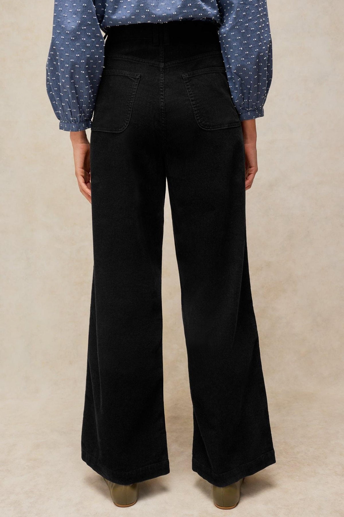 Rear view of a person wearing black corduroy wide-leg trousers paired with a blue patterned shirt.