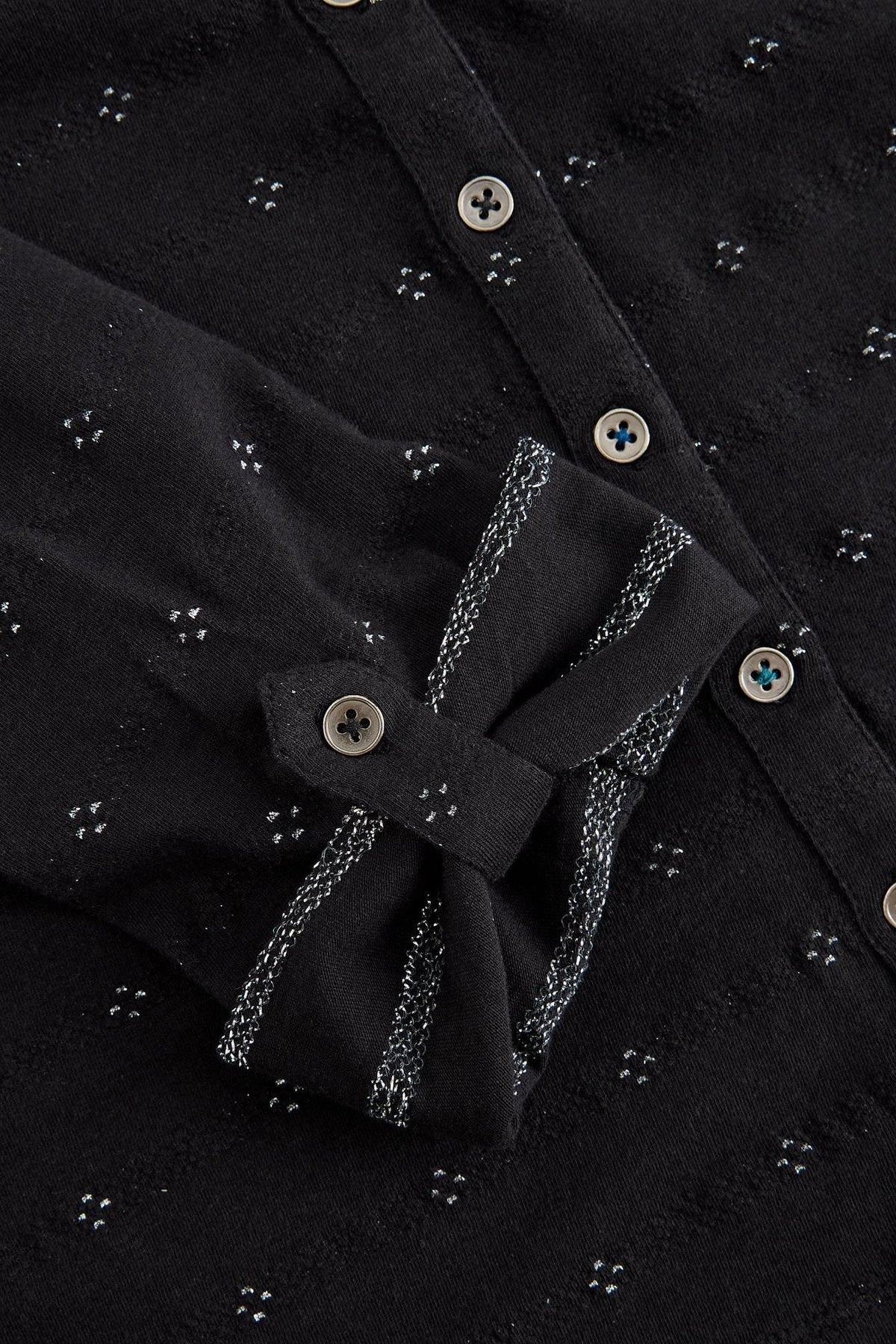 Close-up of a black cotton women's shirt with silver sparkle accents and buttoned cuffs.