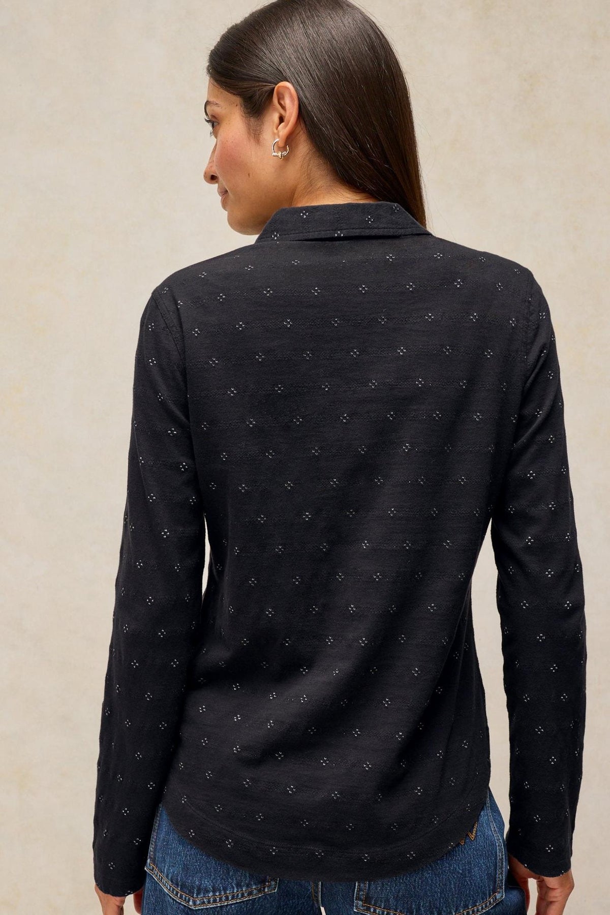 A woman from behind wearing a long-sleeved black cotton shirt with small white sparkle details.