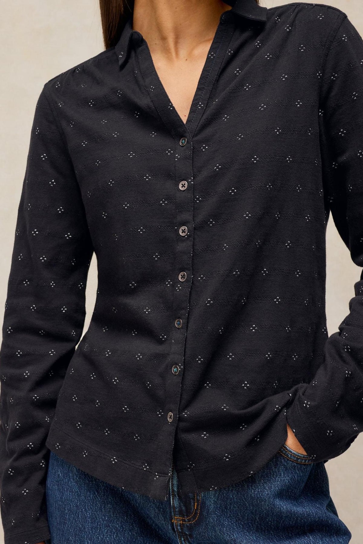 A woman wearing a black long-sleeve cotton shirt with small white sparkle details tucked into blue jeans.