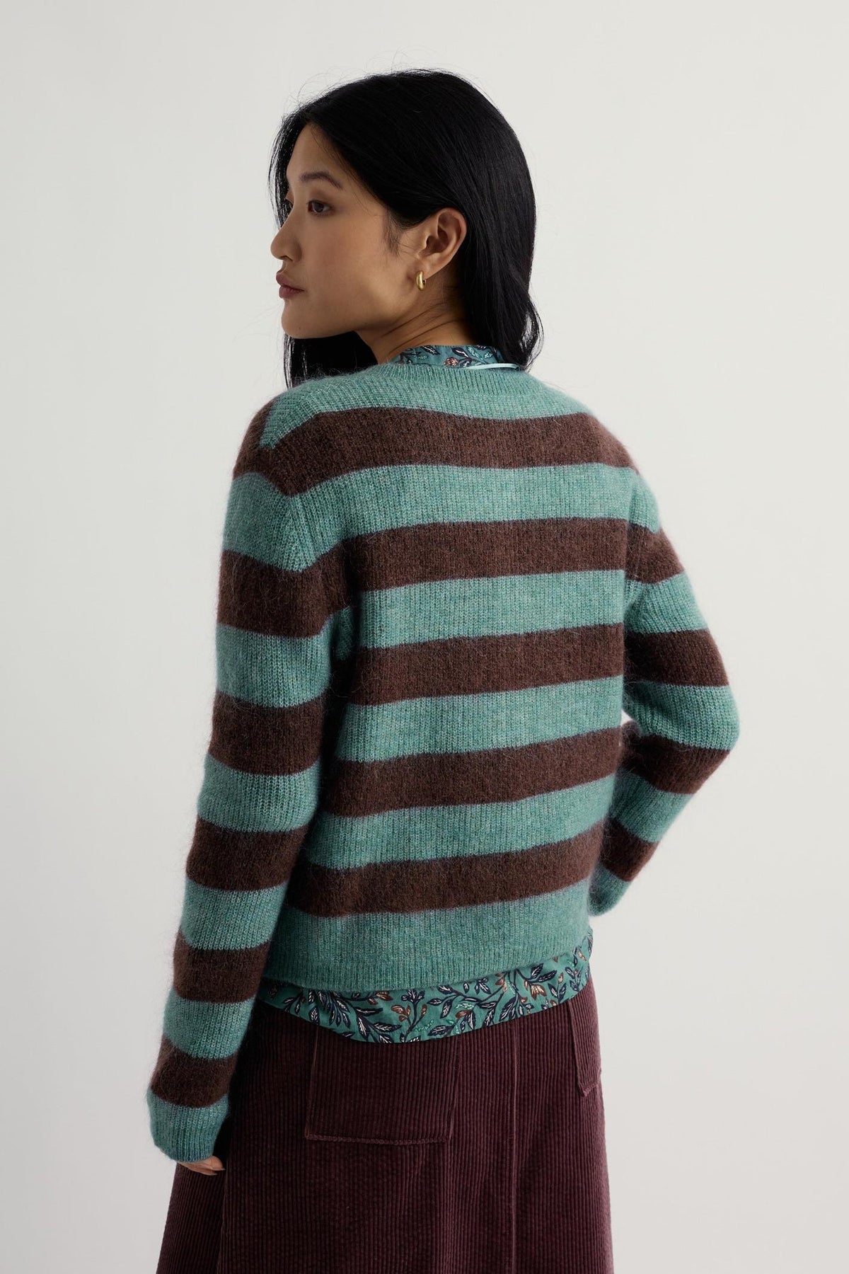 A woman wearing a blue and brown striped mohair knit cardigan viewed from the back.