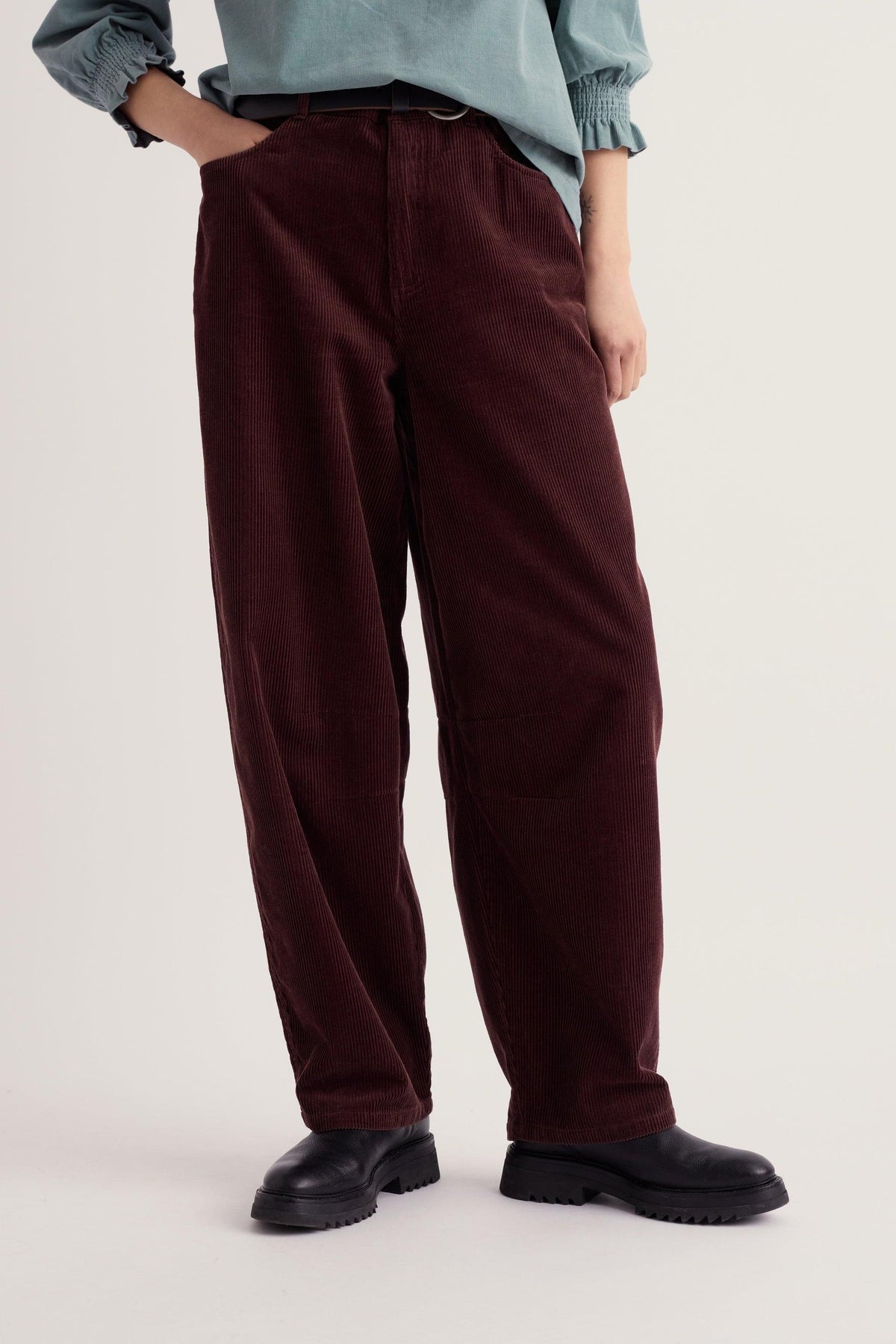 A person wearing brown barrel leg cord trousers and a blue top against a light background.