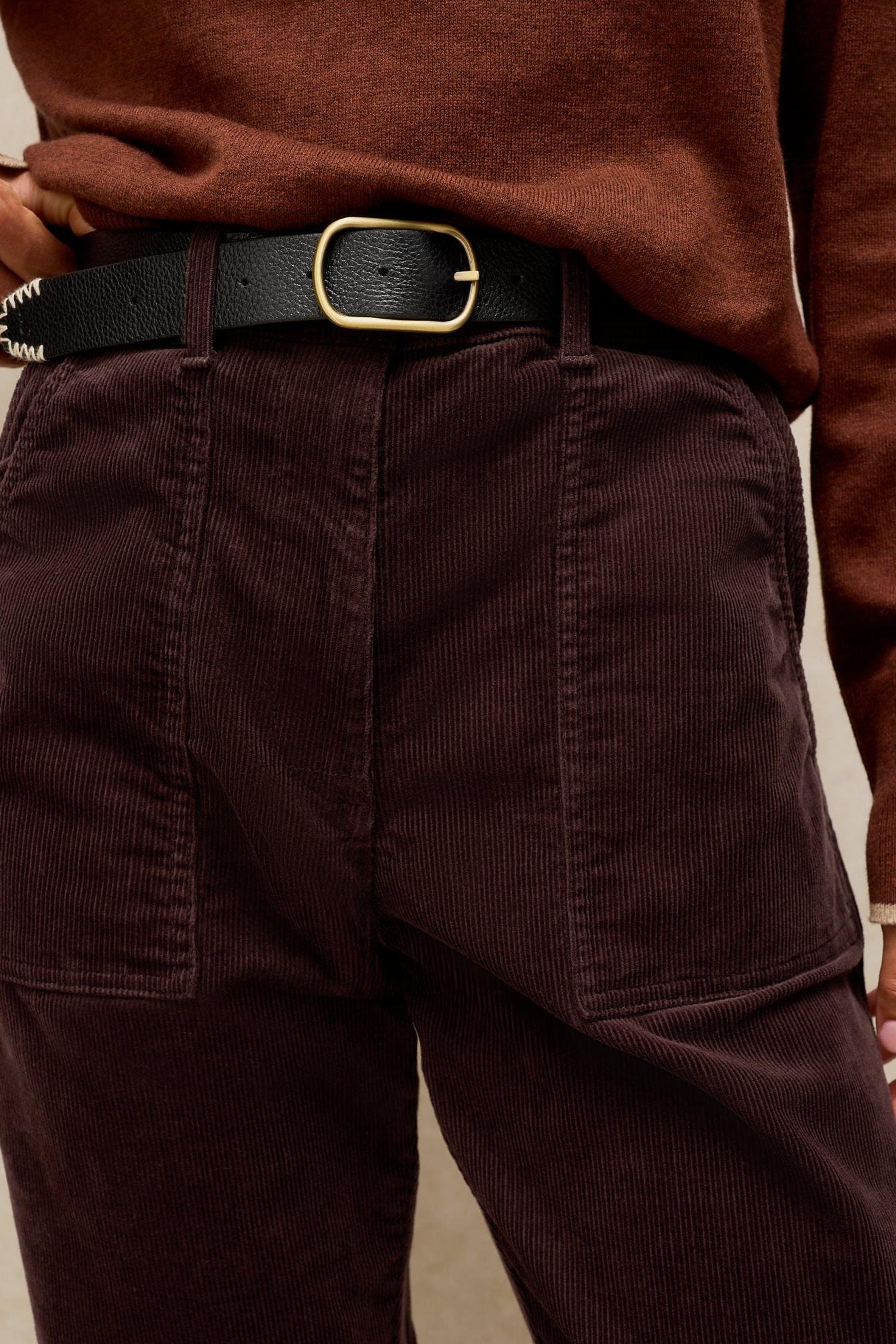 Close up of a woman wearing brown corduroy trousers and a rust-colored sweater with a black belt.