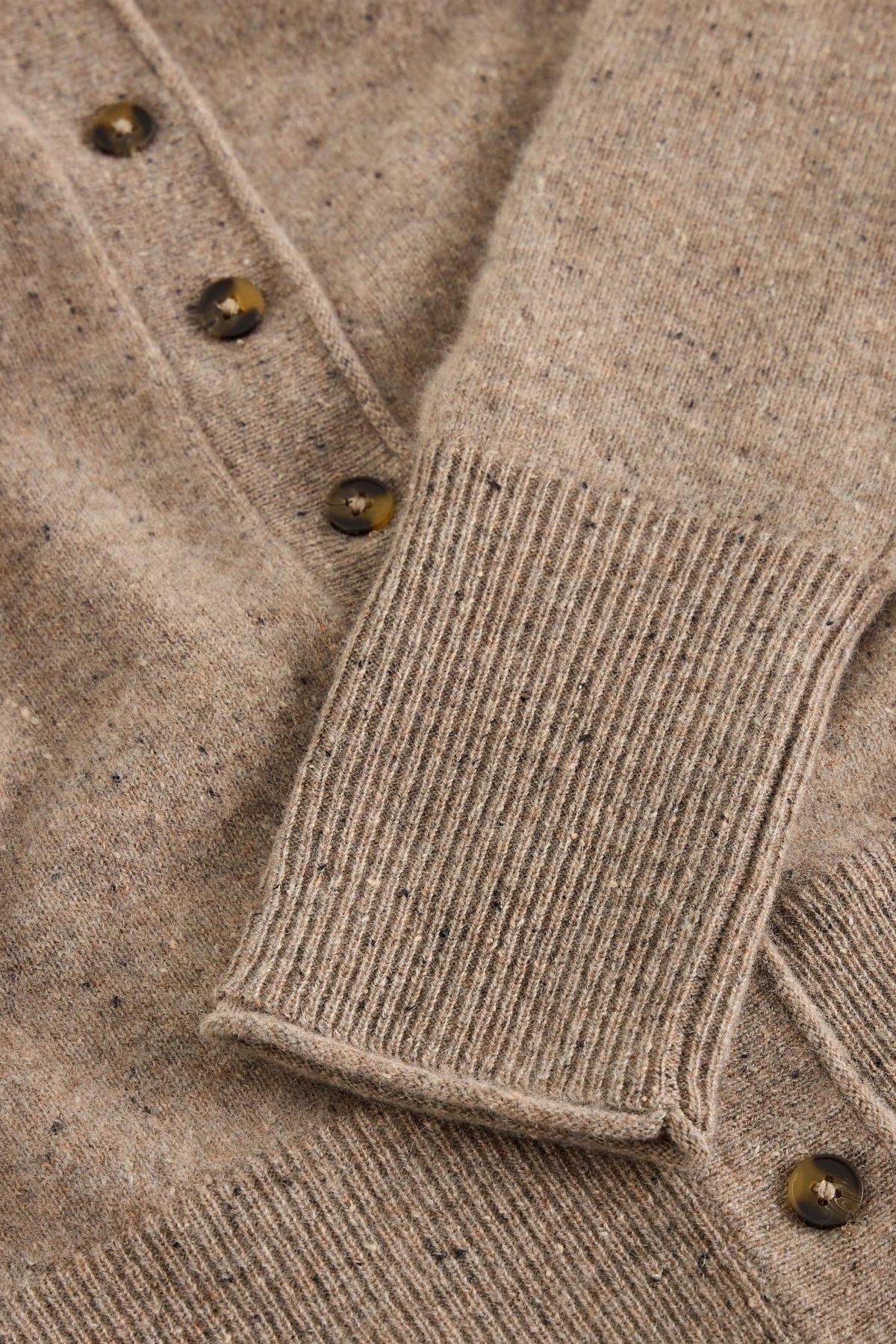 Close-up of a natural-coloured cashmere knit cardigan featuring ribbed cuffs and brown tortoiseshell buttons.