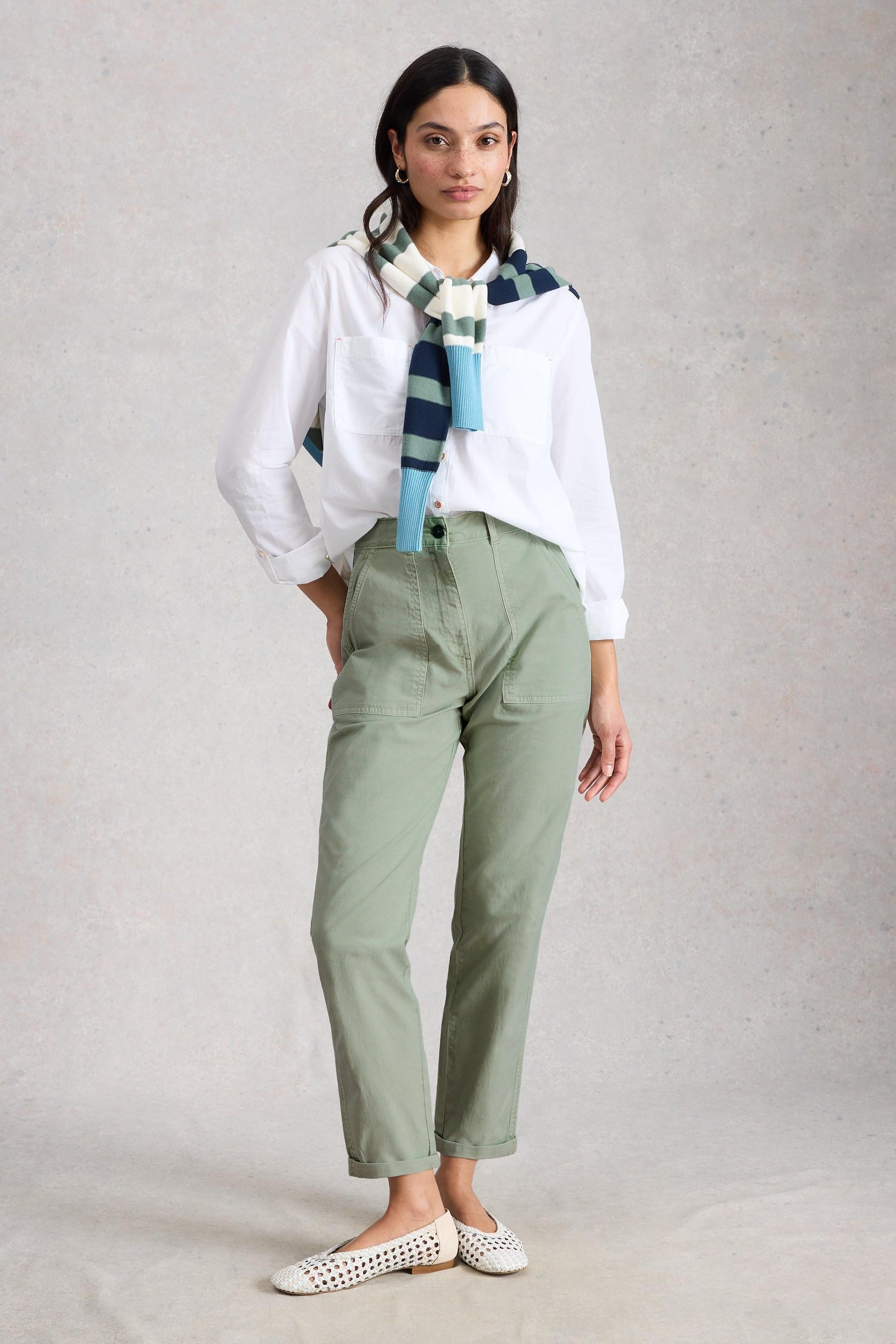 Woman wearing a white shirt, green tapered chinos, and a striped scarf on a plain background