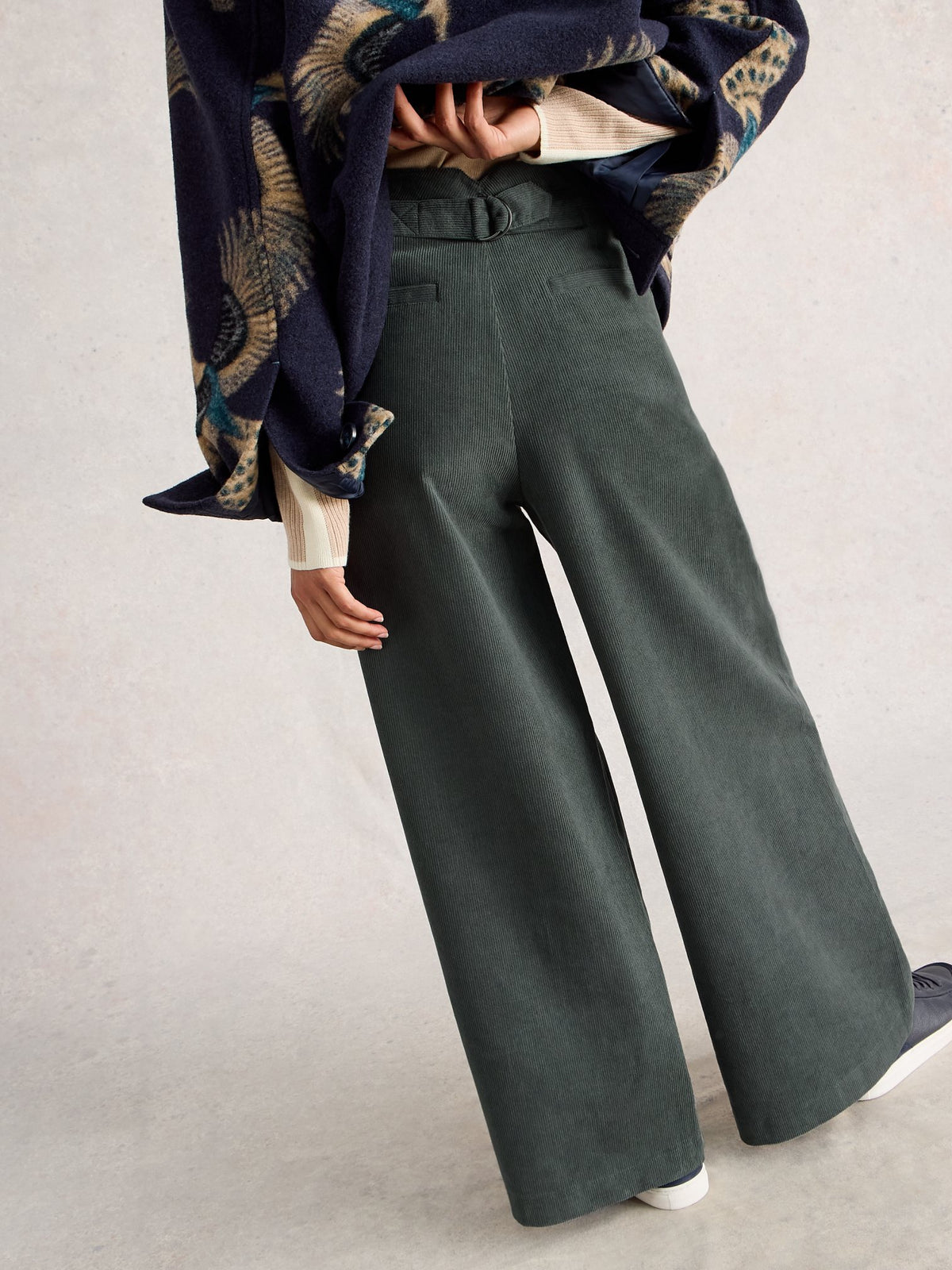 A person wearing dark green wide-leg corduroy trousers paired with a patterned navy jacket.