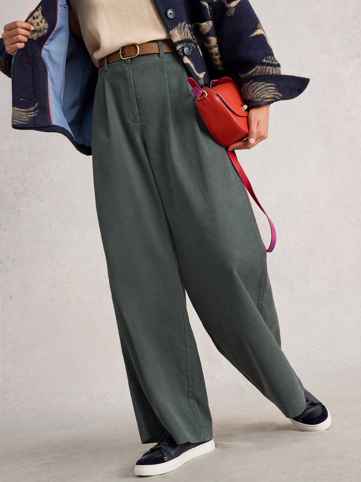 A person wearing long, dark green wide-leg corduroy trousers paired with a cream top and patterned jacket.