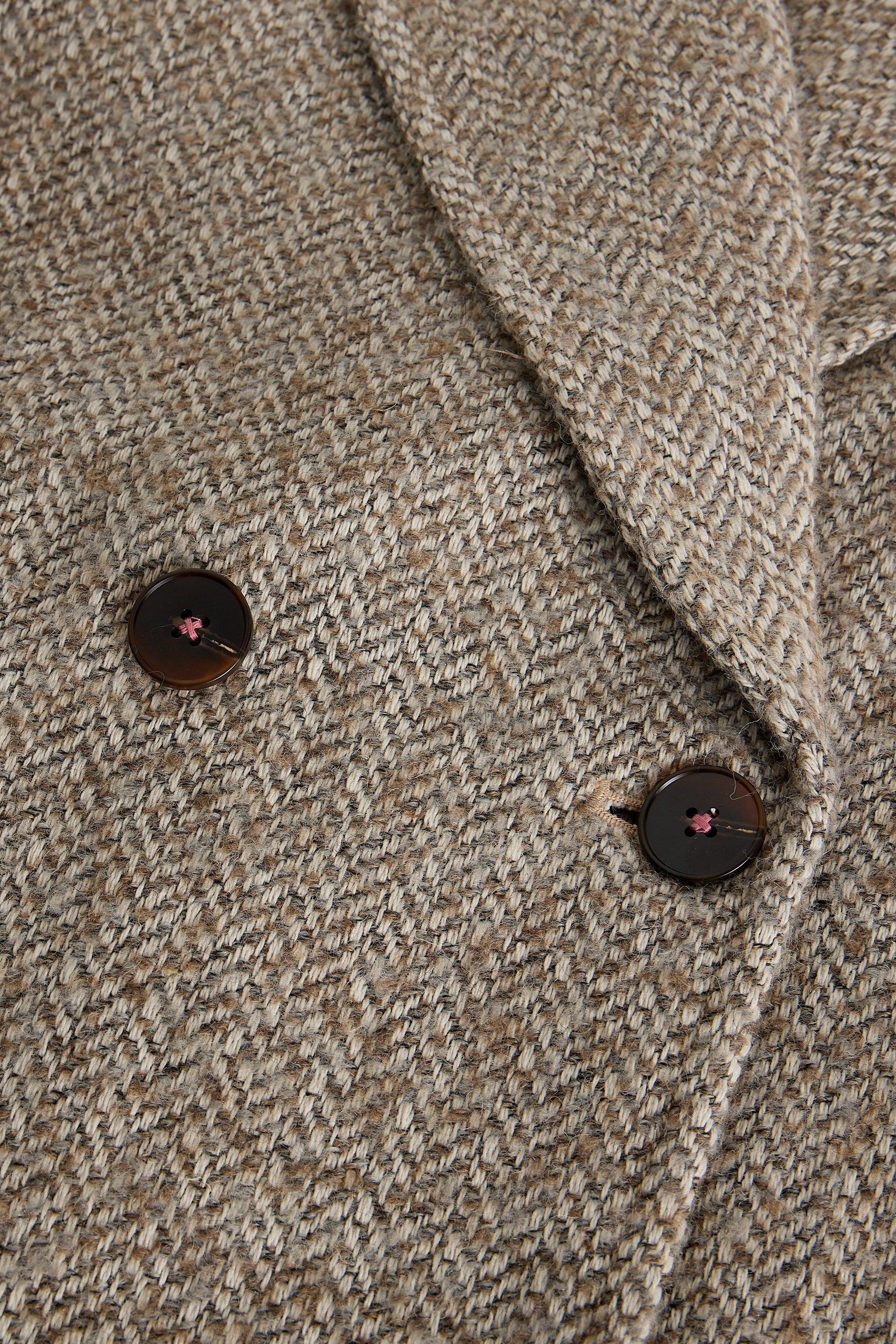 Close-up of a textured beige natural colour wool coat with dark brown buttons.