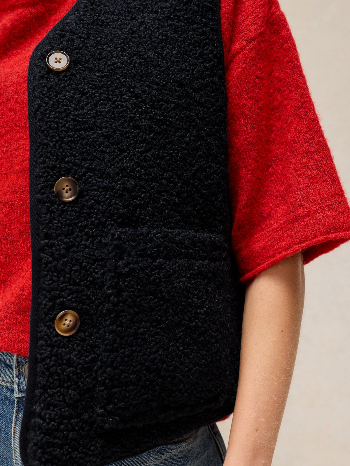 Close-up of a woman wearing a navy blue textured reversible gilet over a bright red sweater.
