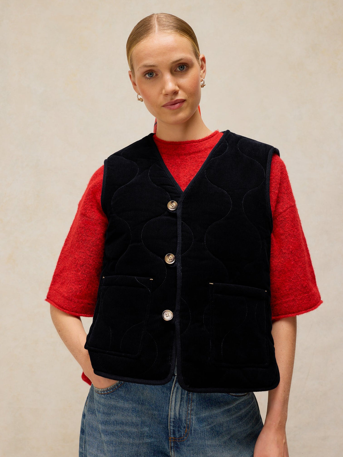 A woman wearing a navy blue quilted reversible gilet over a red sweater against a neutral background.