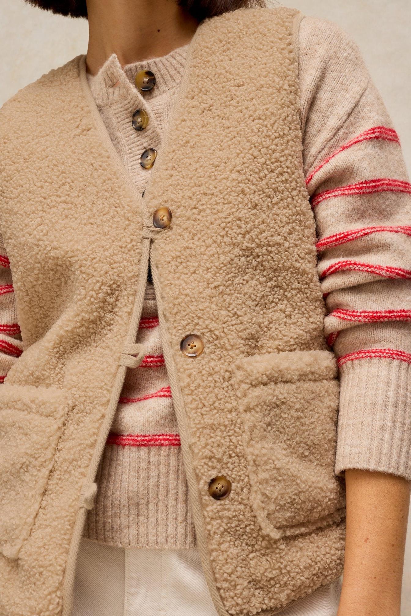 A woman wearing a cosy neutral colour fleece gilet over a striped sweater as an outer layer.