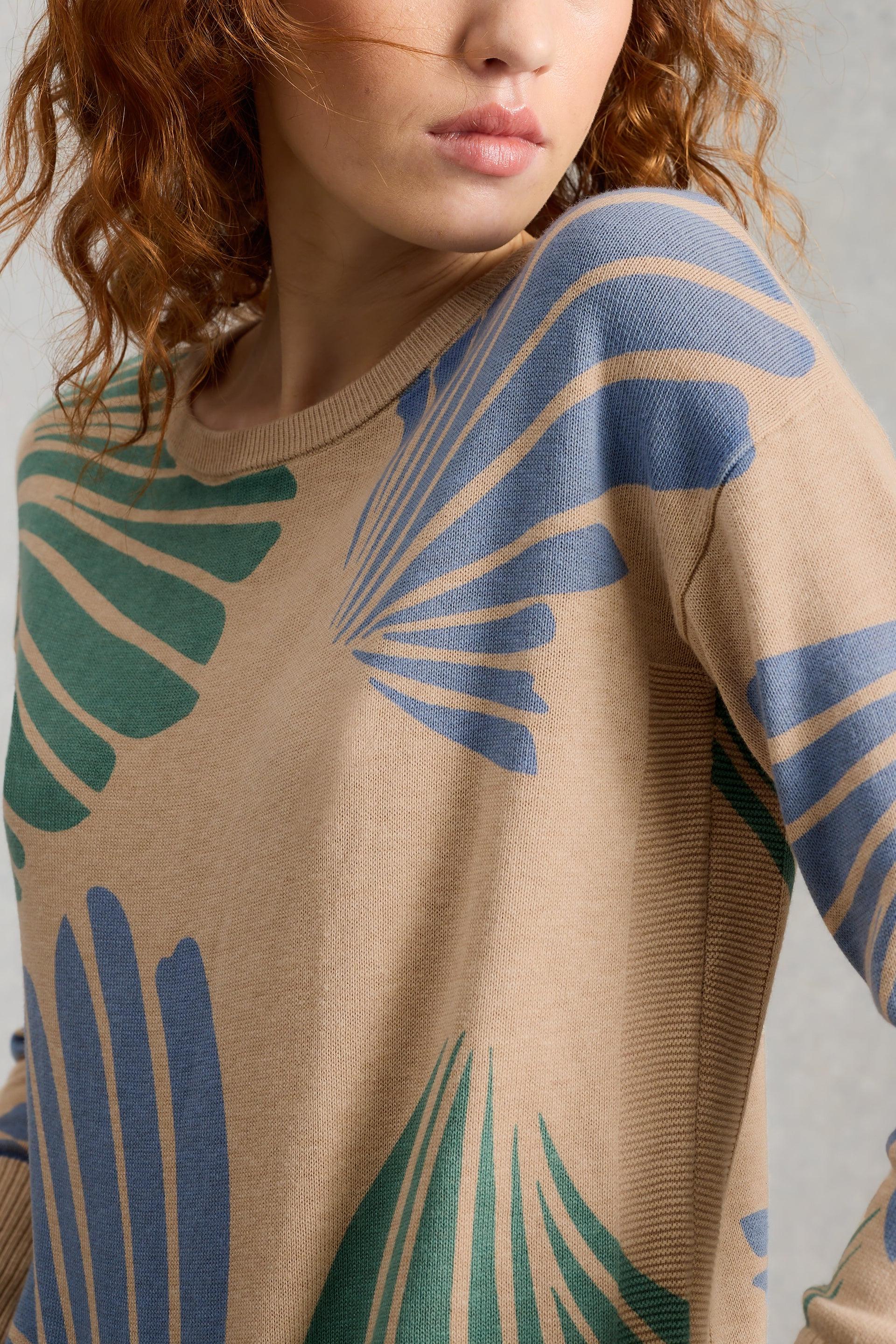 Person wearing a beige organic cotton sweater with blue and green leaf patterns.