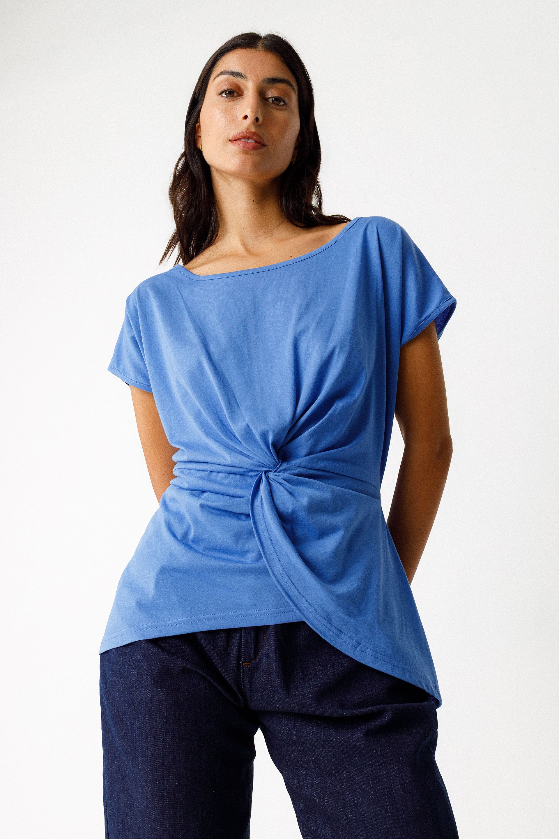 Woman wearing a blue organic cotton top with a knot detail on a white background