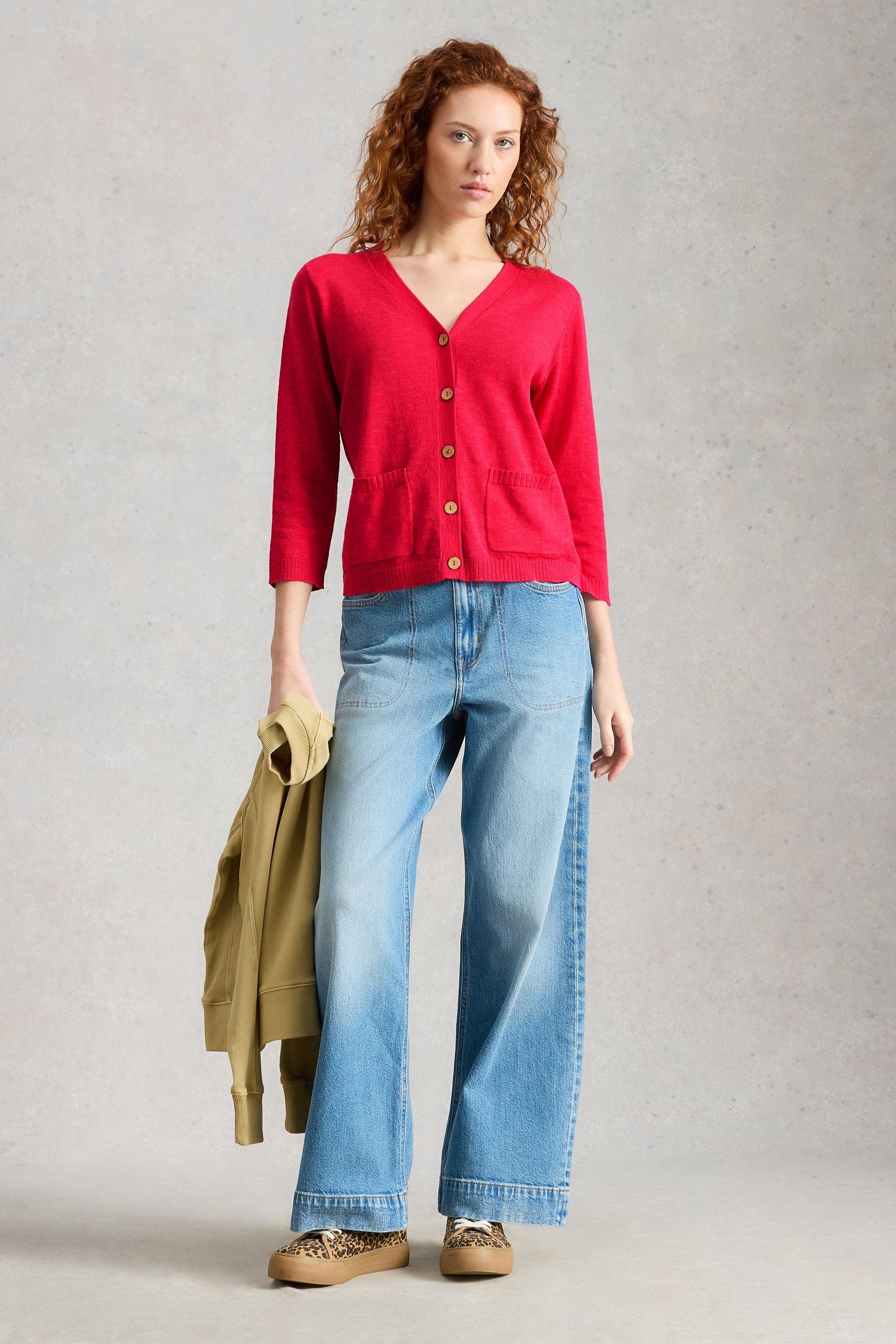 Woman wearing a pink organic cotton cardigan and blue jeans on a plain background
