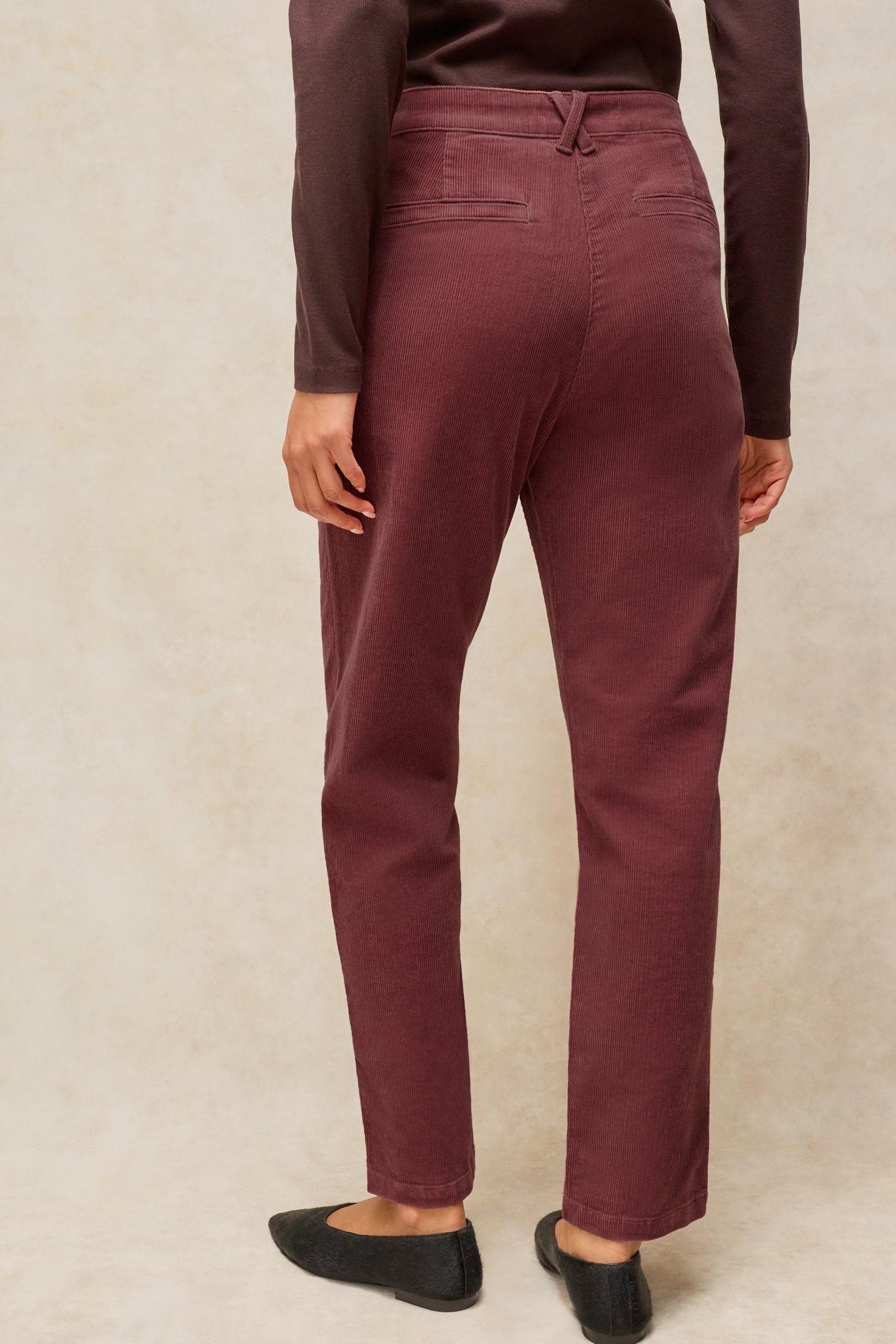 Rear view of a woman wearing pink corduroy trousers made of organic cotton against a neutral background.