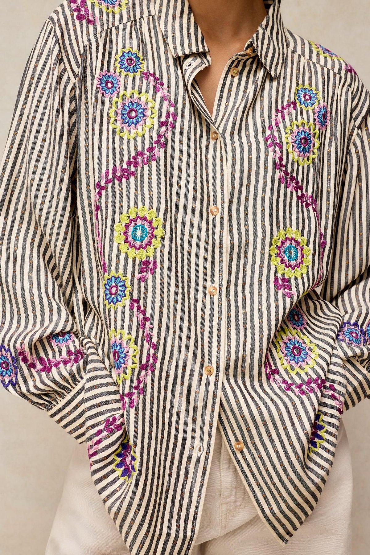 A woman wearing a White Stuff striped blouse featuring vibrant purple and green floral embroidered patterns.
