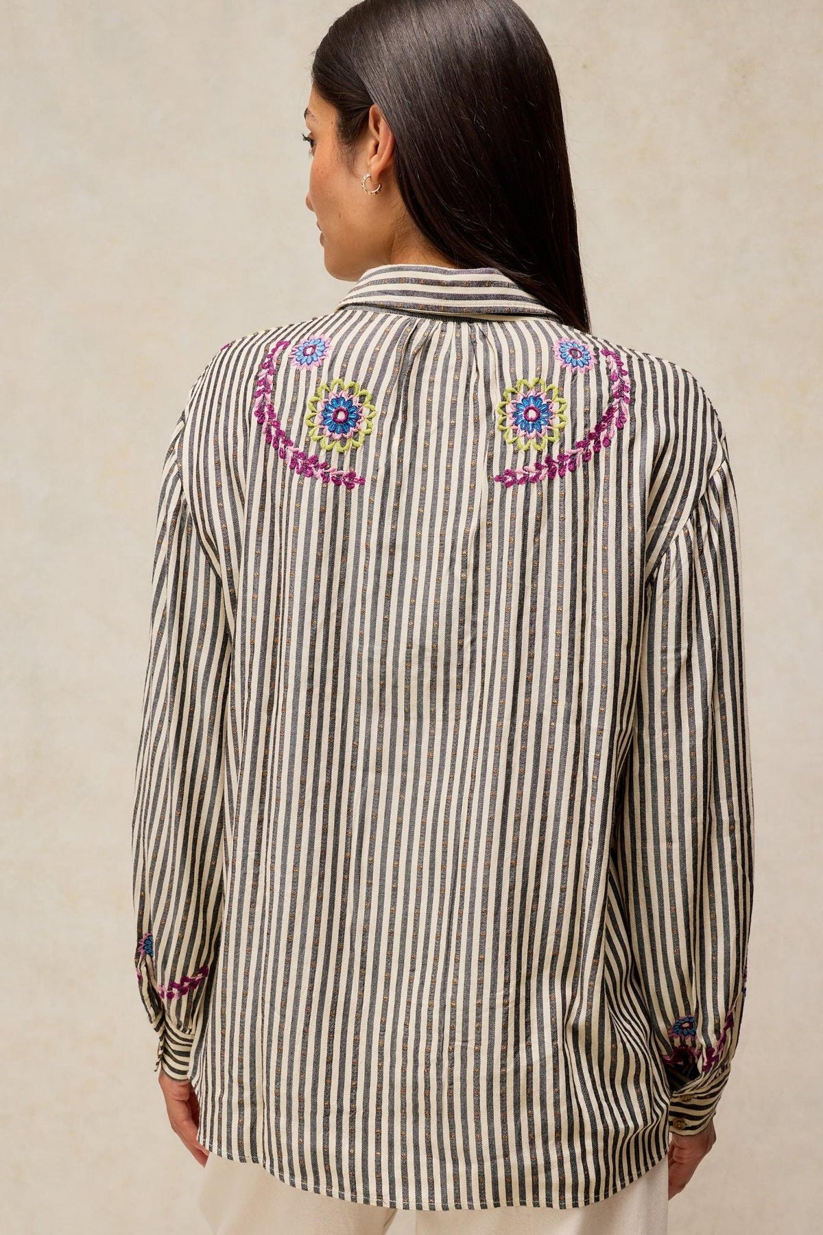 Woman wearing a White Stuff long-sleeved striped blouse with colorful floral embroidery on the back.