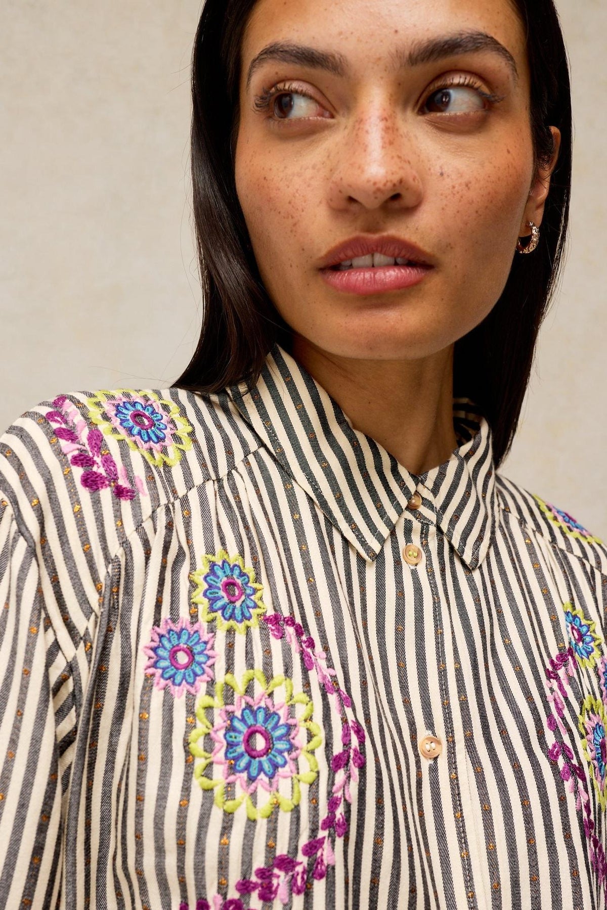 A woman wearing a White Stuff striped blouse with colorful floral embroidery details.