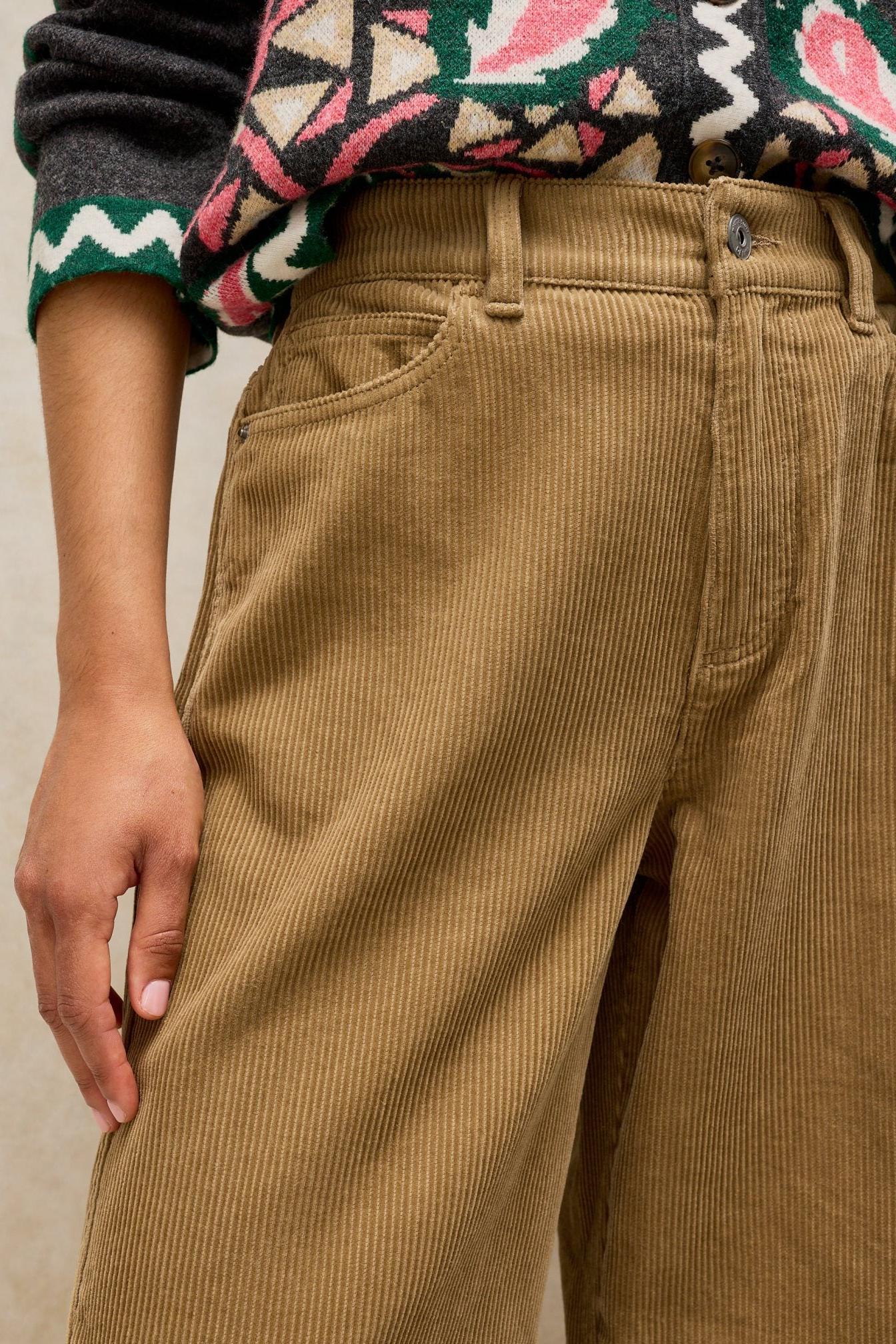 Close up of a woman wearing tan corduroy trousers paired with a patterned cardigan.
