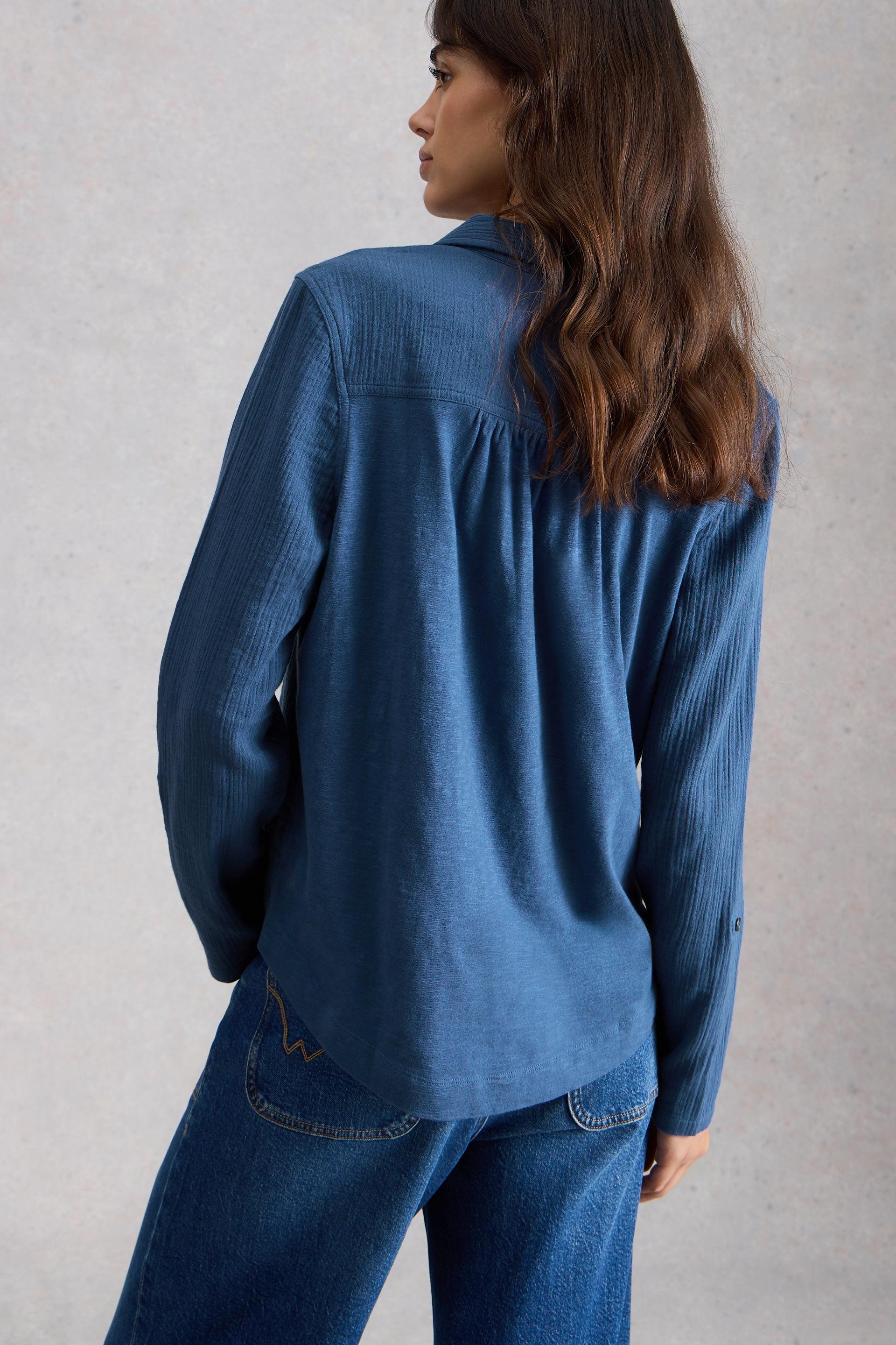 Woman wearing a blue organic cotton shirt and jeans against a gray background