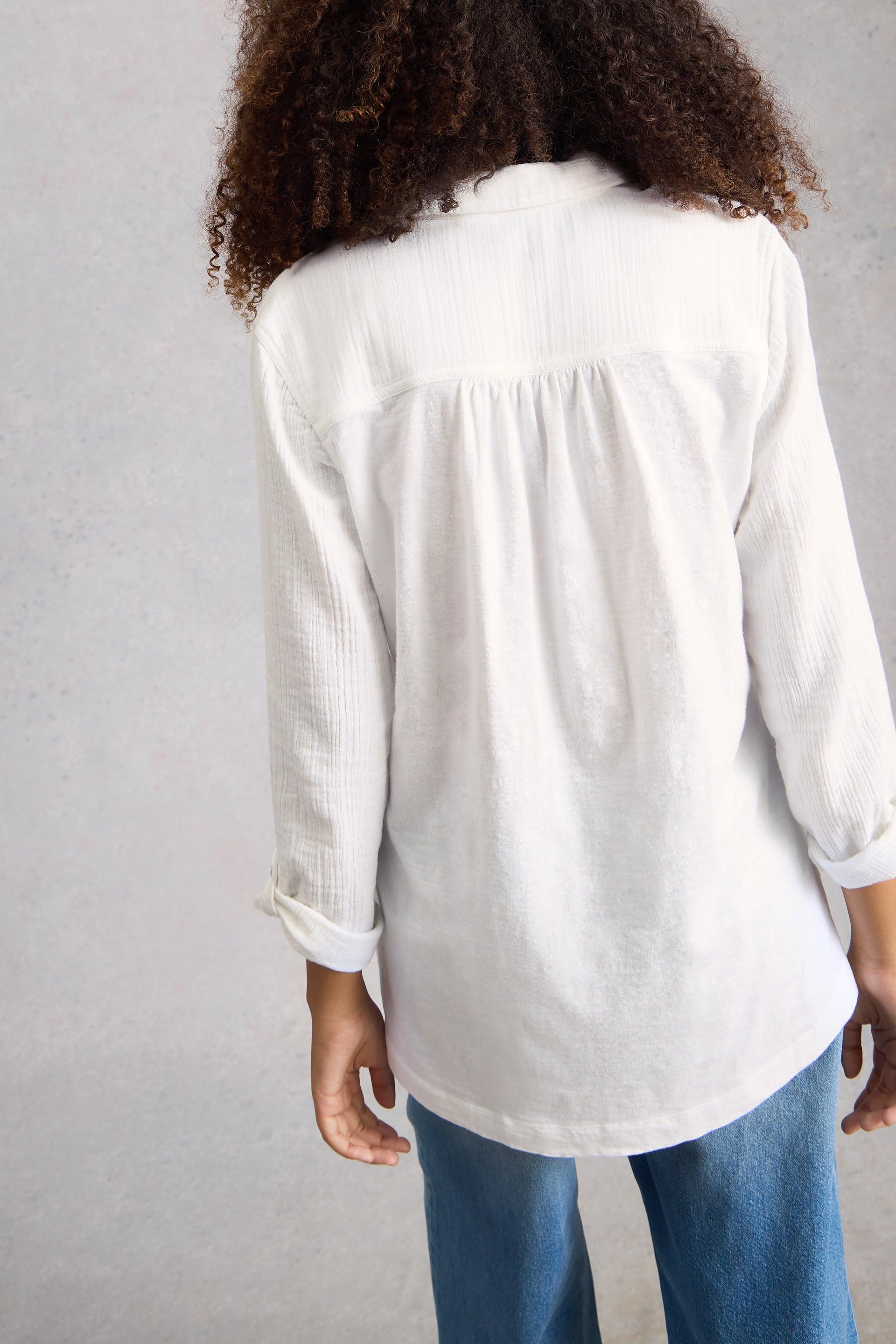 Person wearing a white organic cotton blouse and blue jeans against a gray background