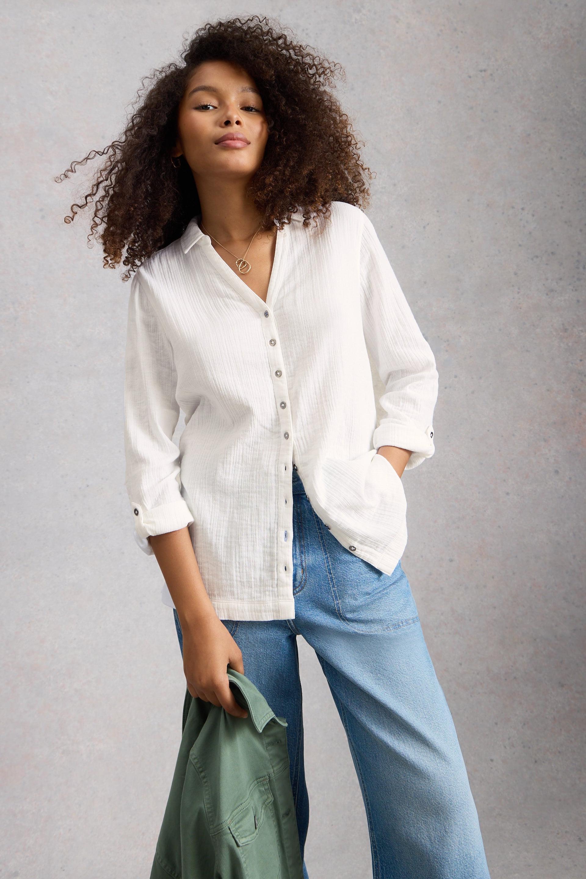 Woman wearing a white button-up shirt and blue jeans against a gray background