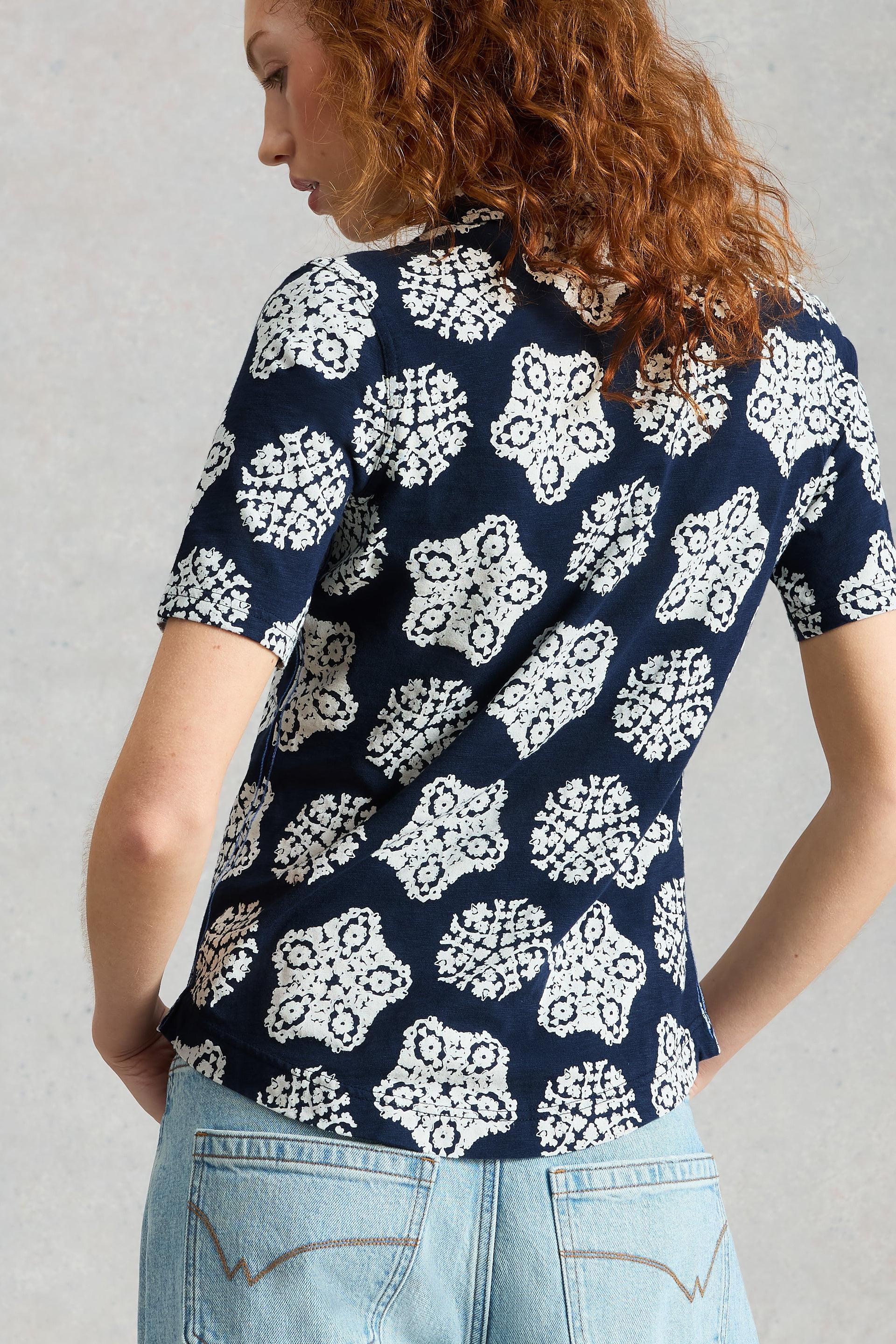 Woman wearing a navy blue top with white floral pattern against a gray background