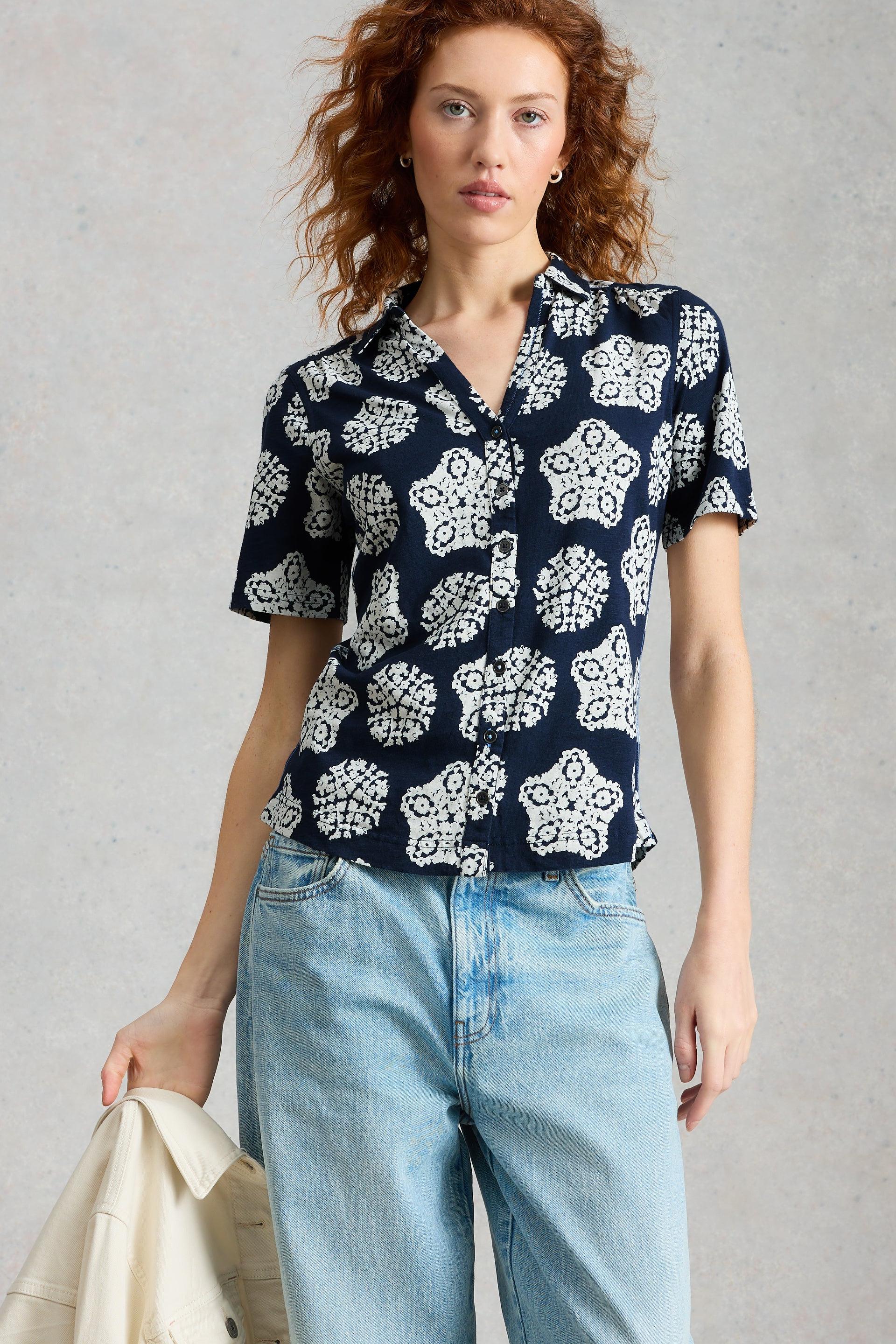 Woman wearing a navy blue floral patterned shirt and light blue jeans against a gray background