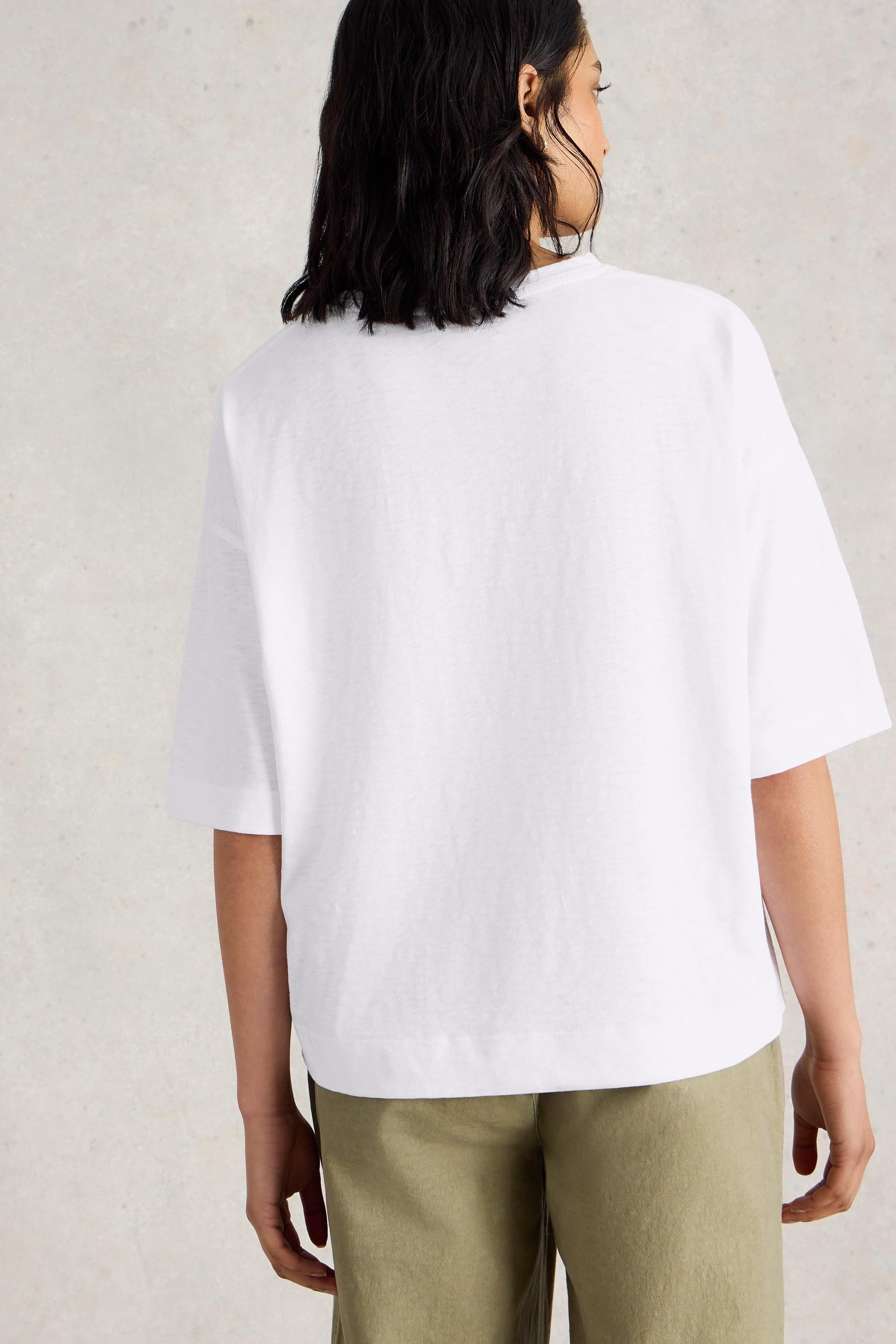 Person wearing a white cotton t-shirt and green pants on a plain background