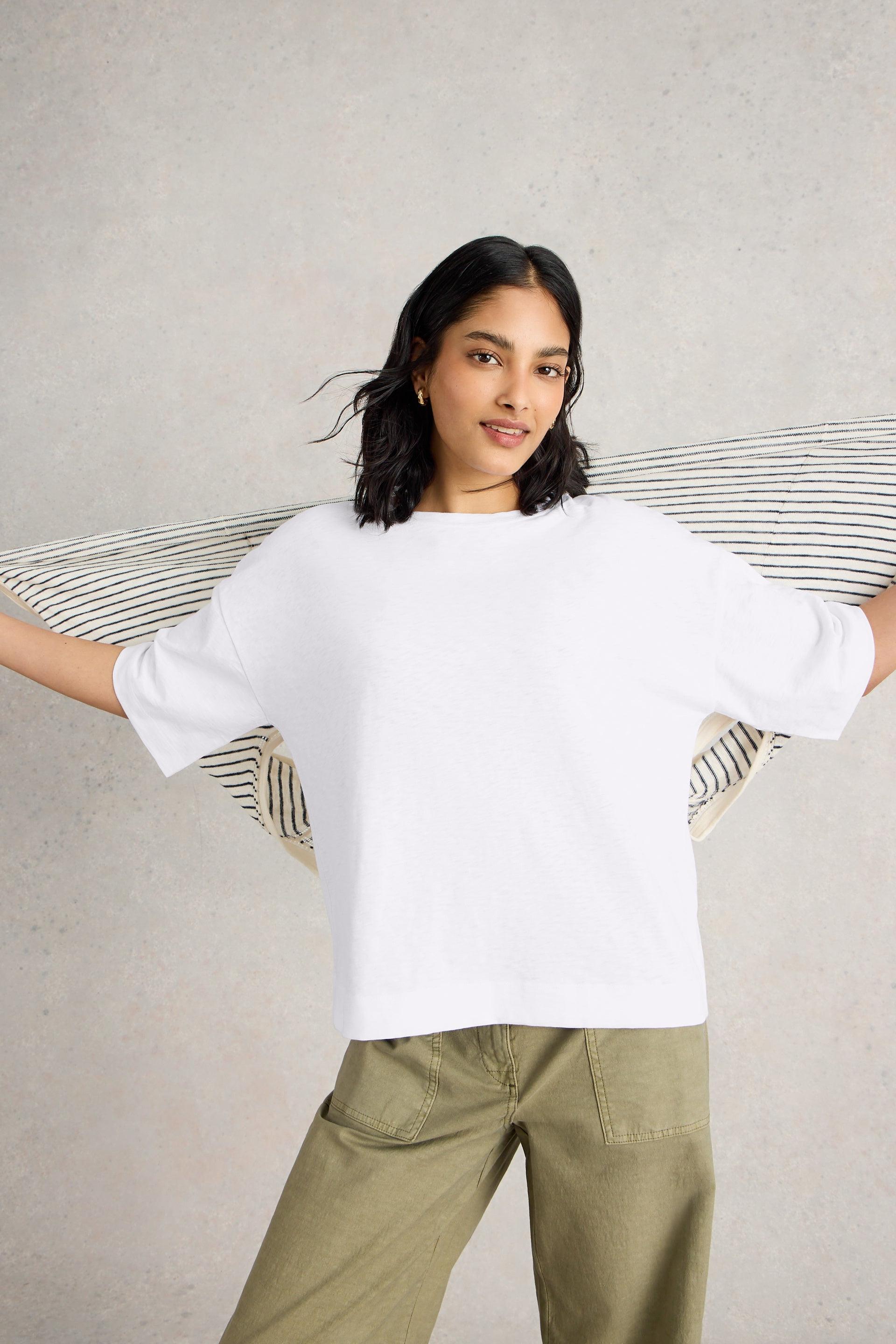 Woman wearing a white cotton t-shirt and green pants against a neutral background