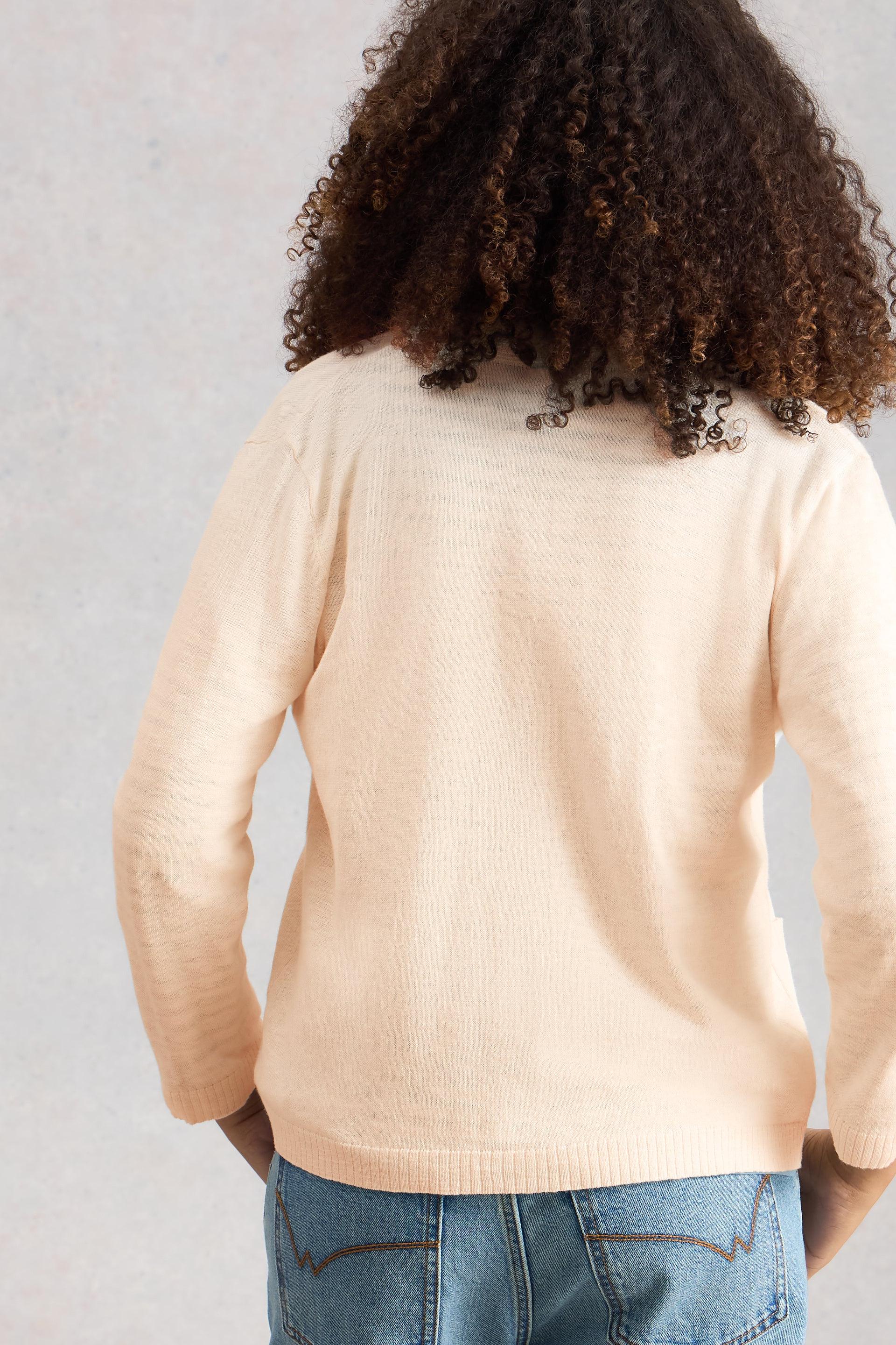Person wearing a beige White Stuff cardigan and blue jeans against a light gray background