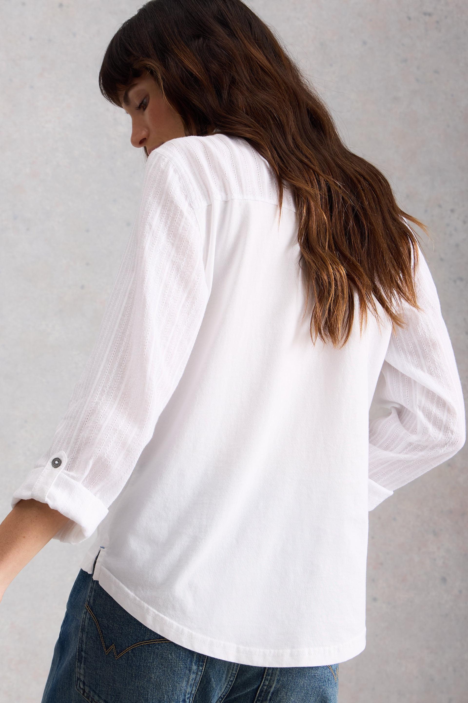 Woman wearing a white cotton shirt and blue jeans against a gray background
