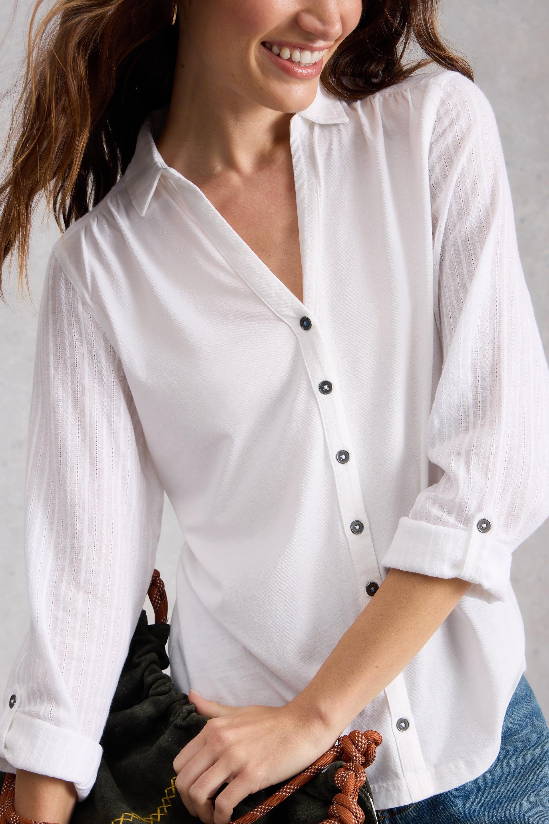 Woman wearing a white button-up shirt with rolled-up sleeves, holding a black handbag.