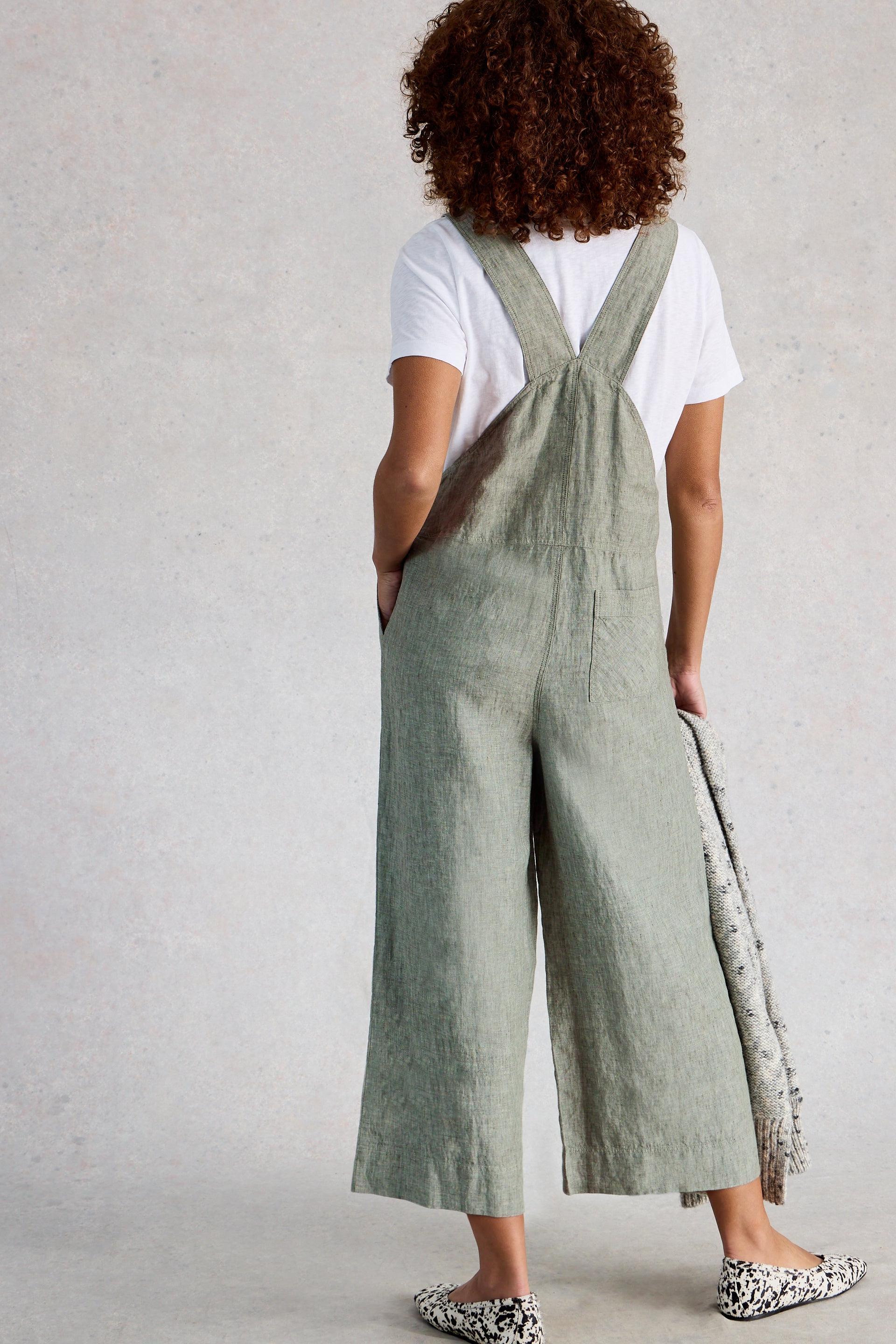 Person wearing green linen jumpsuit and a white shirt against a plain background