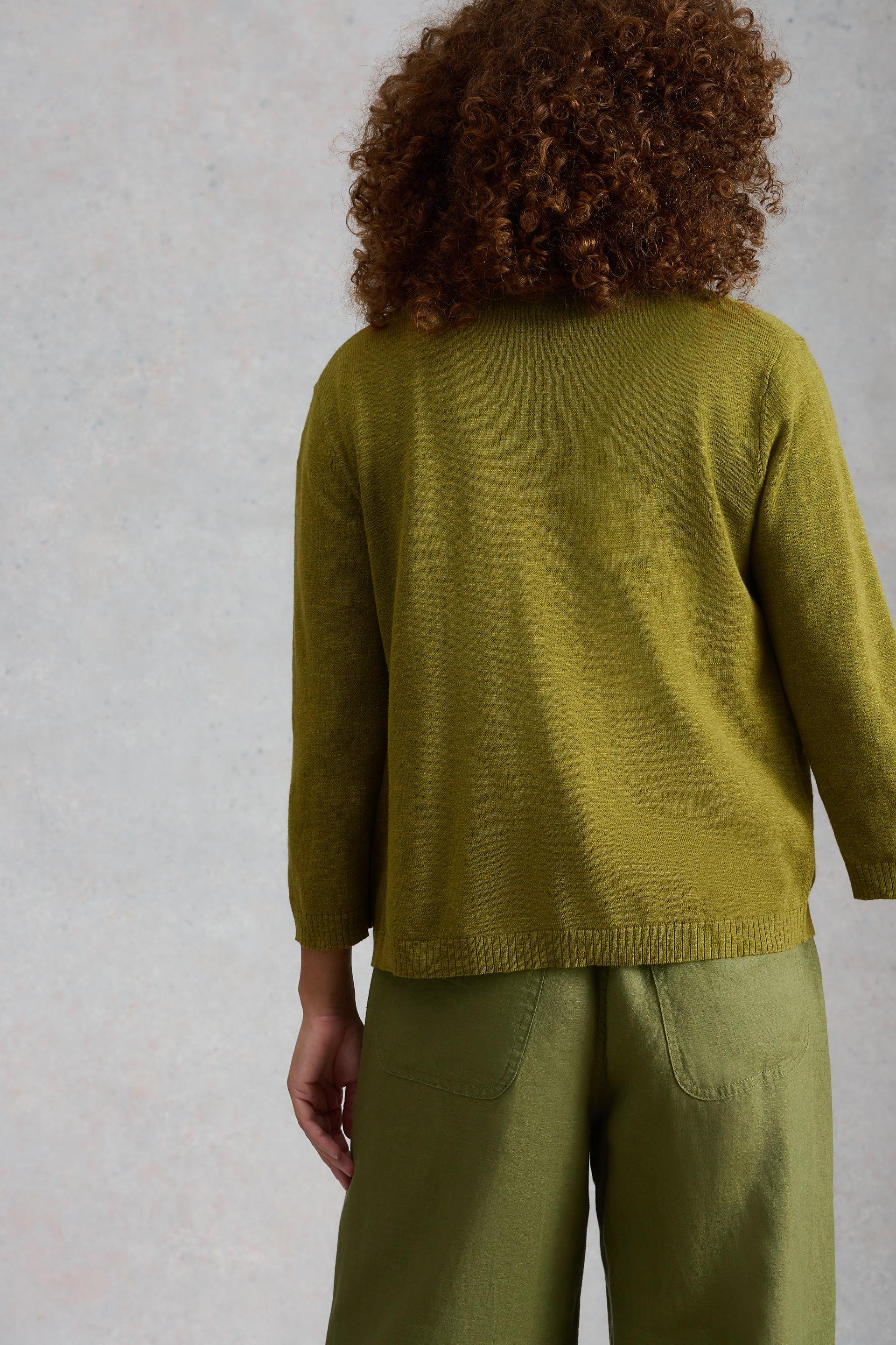 Person wearing a green organic cotton cardigan and pants against a neutral background