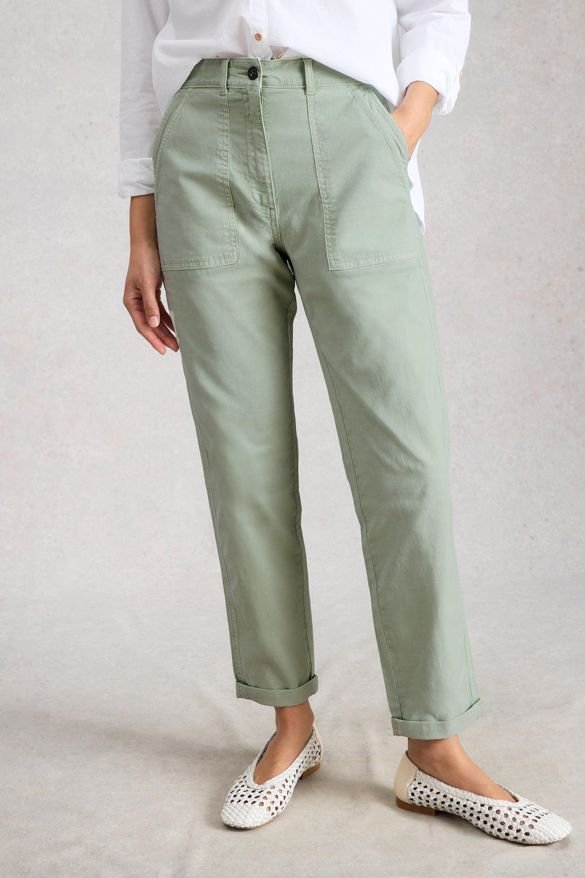 Person wearing light green tapered chino pants and white shoes on a plain background