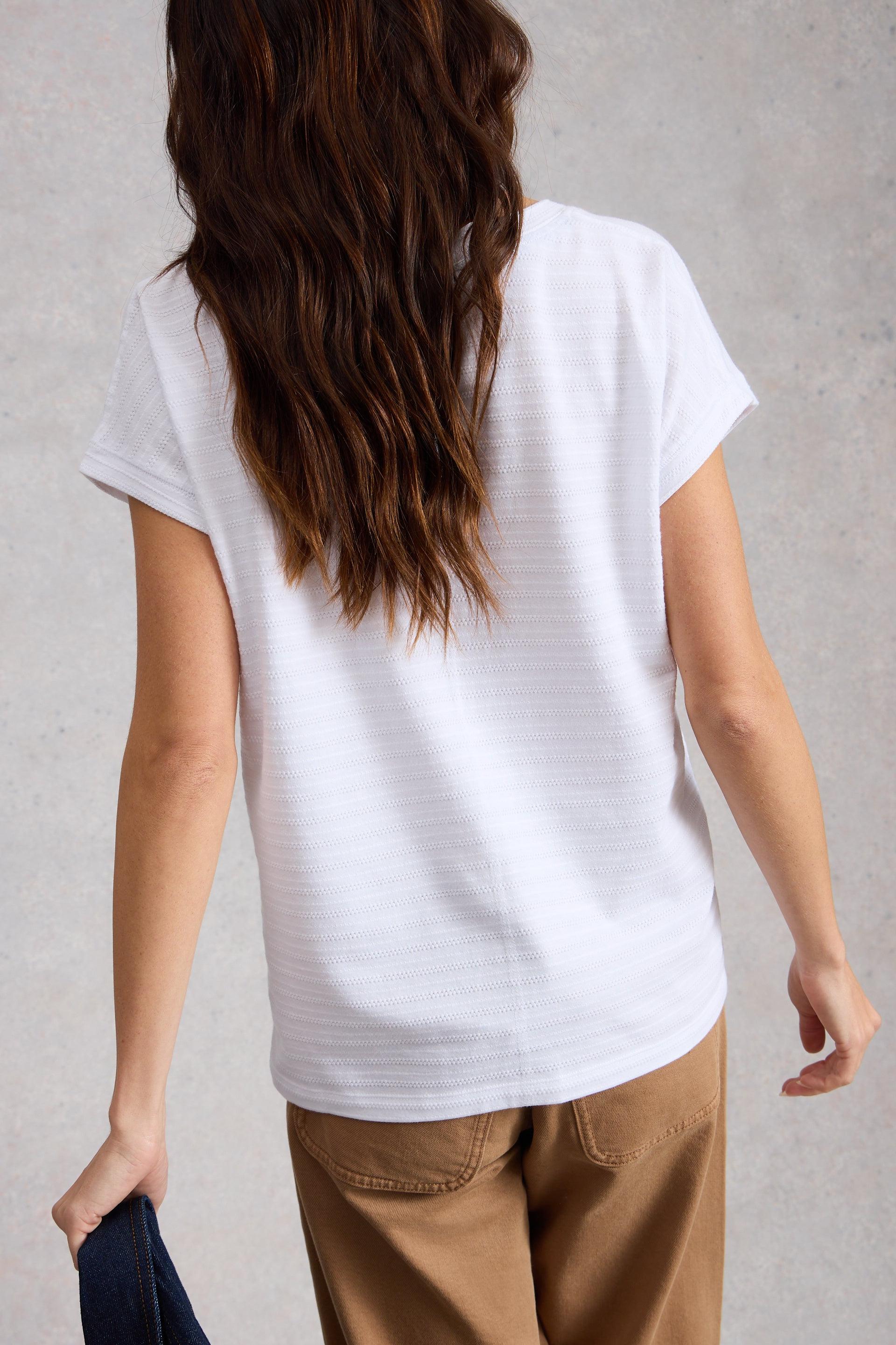 Person wearing a plain white t-shirt and brown pants against a gray background