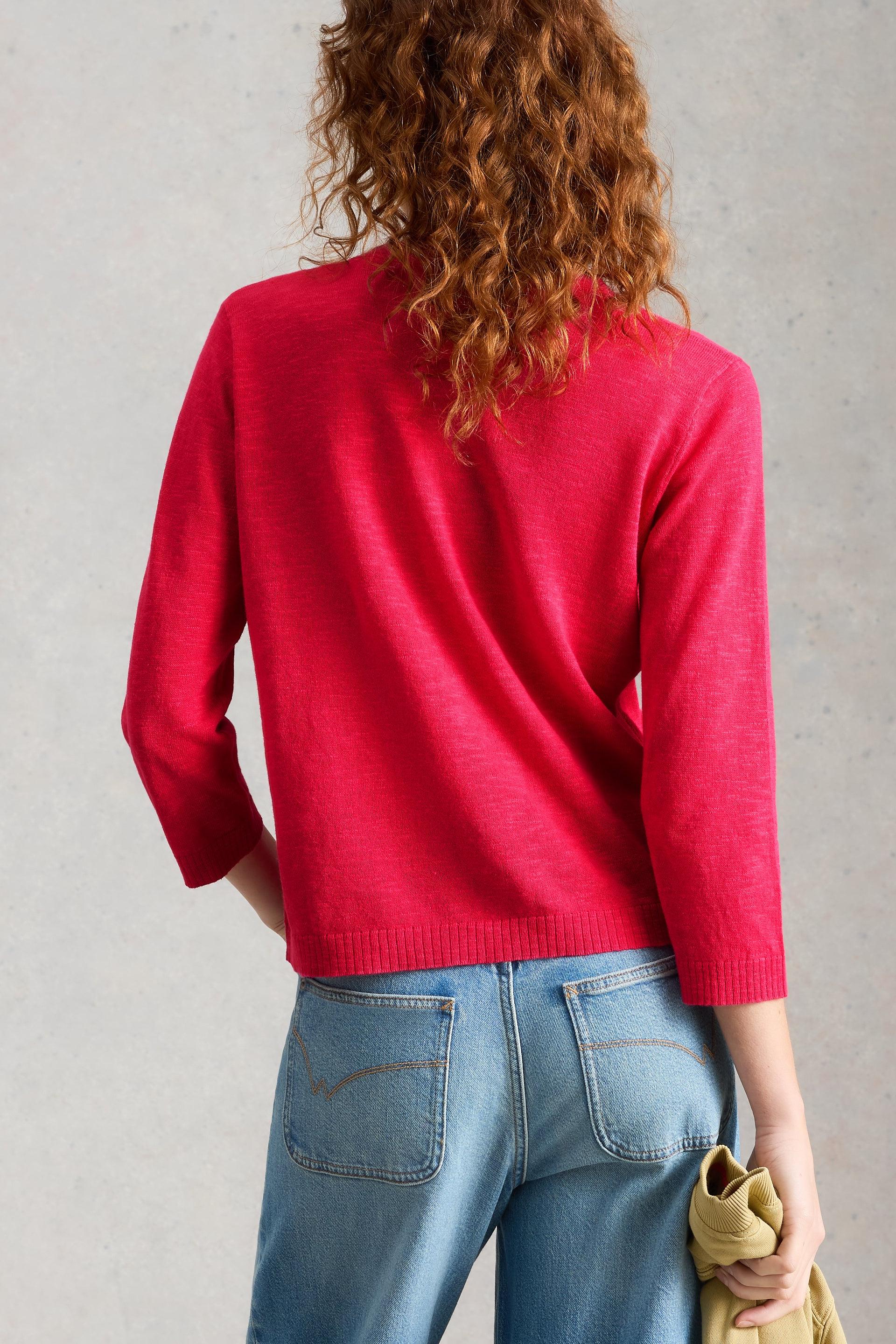 Back view of model wearing a pink organic cotton cardigan and blue jeans against a gray background