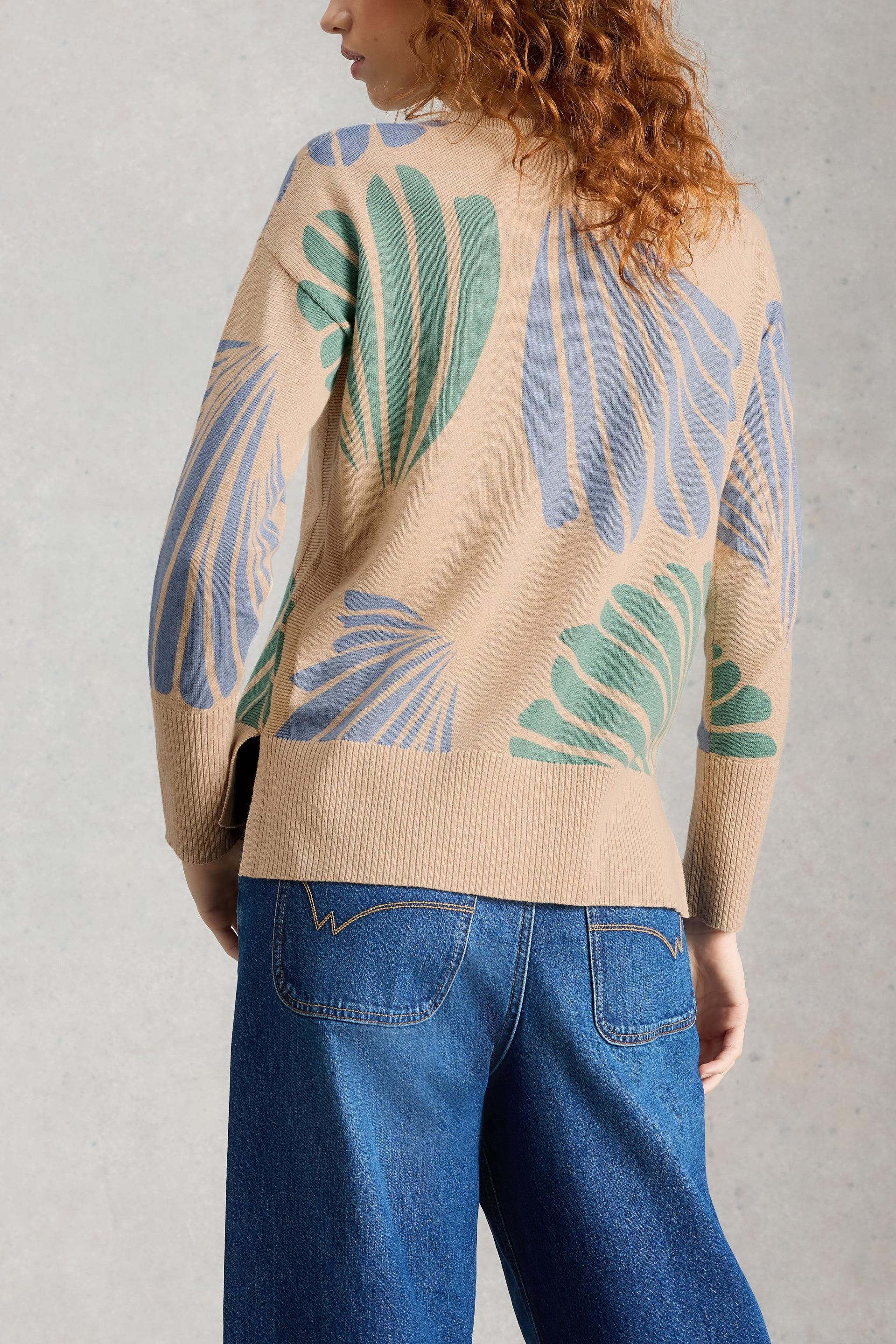 Person wearing a beige organic cotton sweater with leaf pattern and blue jeans against a gray background