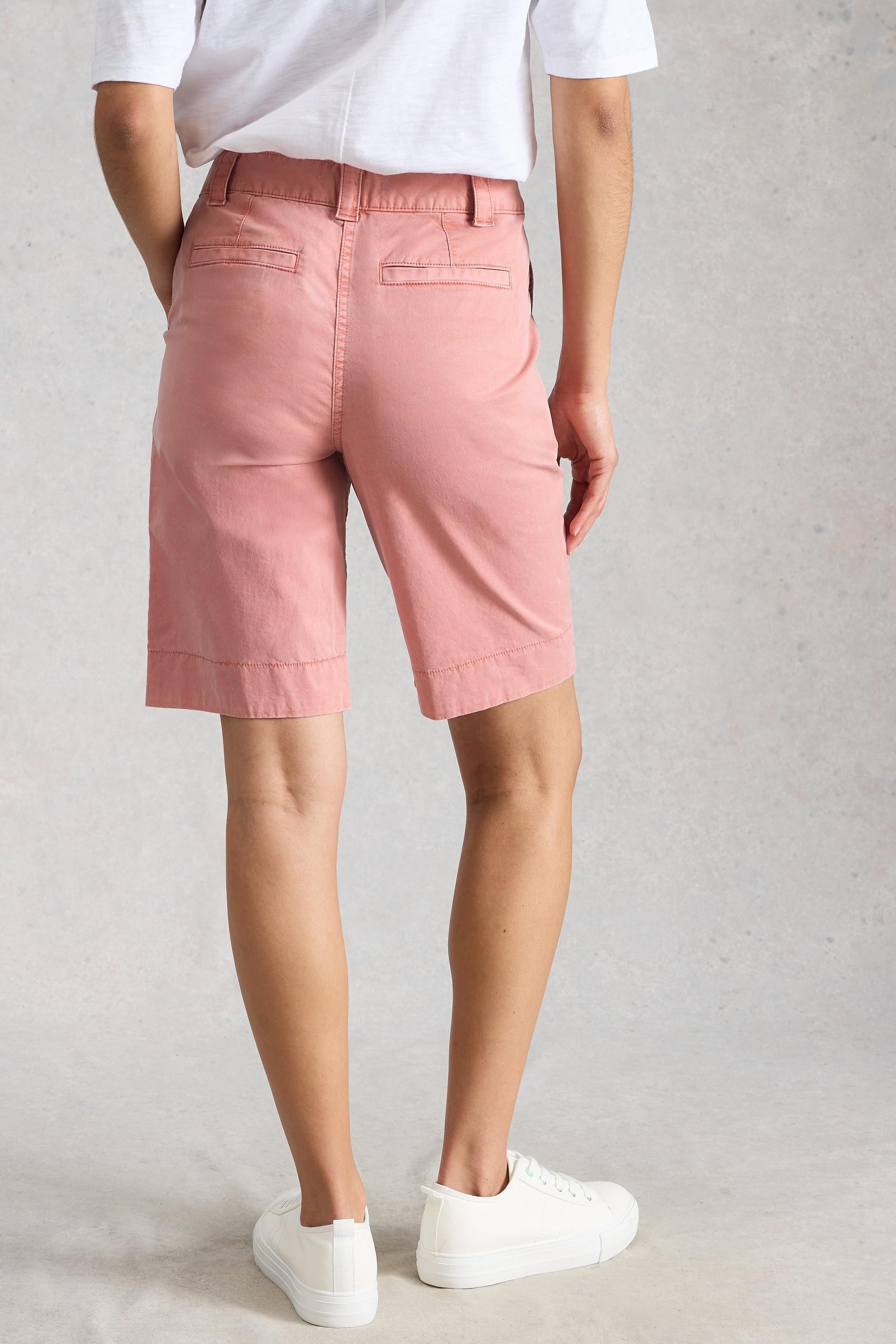 Person wearing pink shorts and white shoes on a plain background