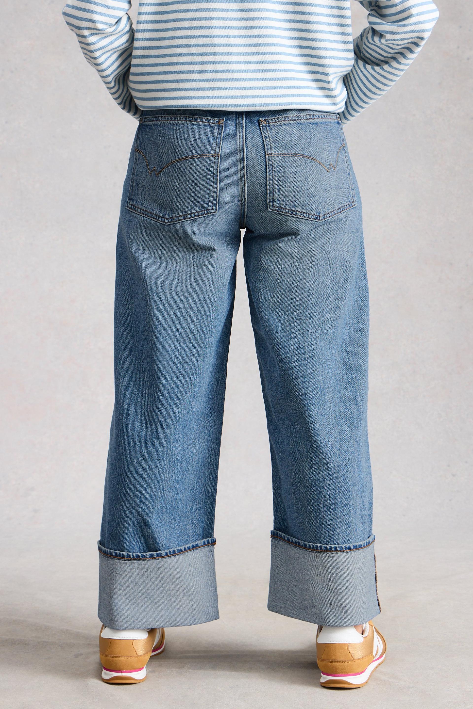 Back view of model wearing blue jeans with turn up and a striped shirt with a neutral background