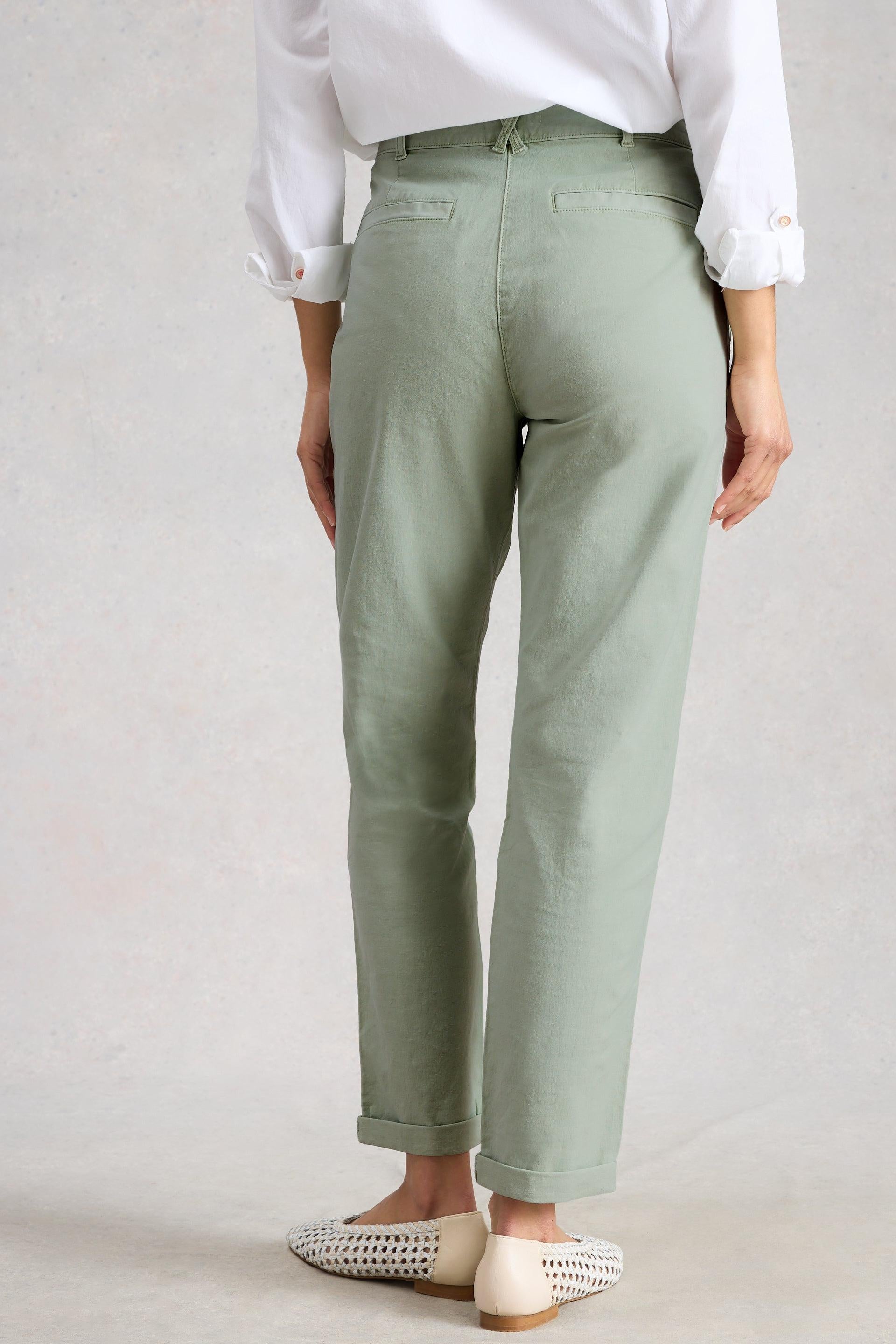 Person wearing light green organic cotton pants and a white shirt on a plain background