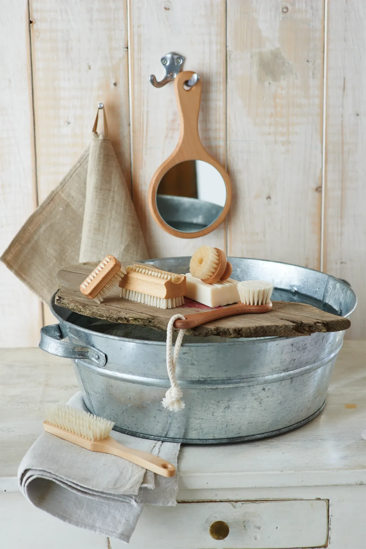 Metal bath tub with soap, brush, and towel on a wooden surface