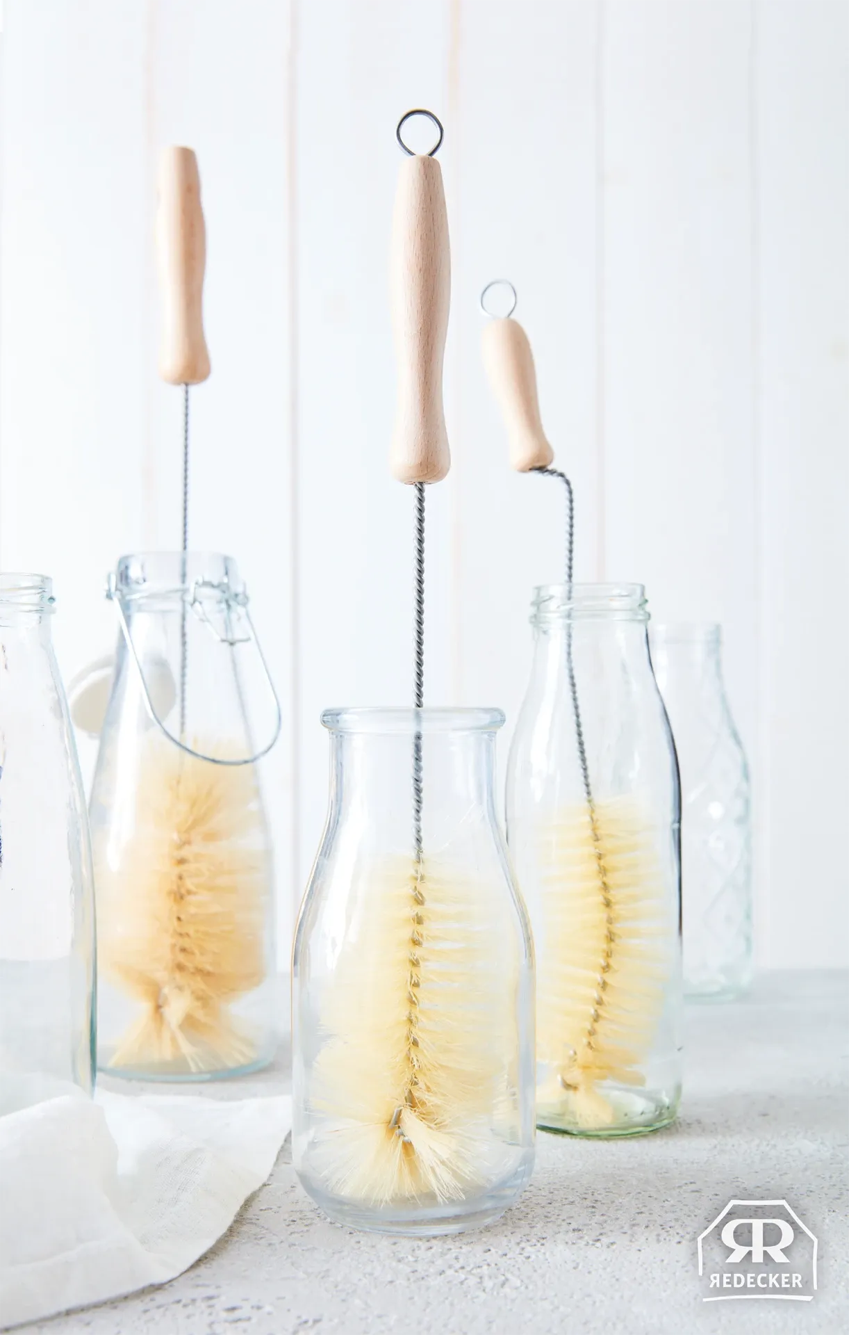 Clear glass bottles with wooden handles and bristle brushes inside on a white surface.