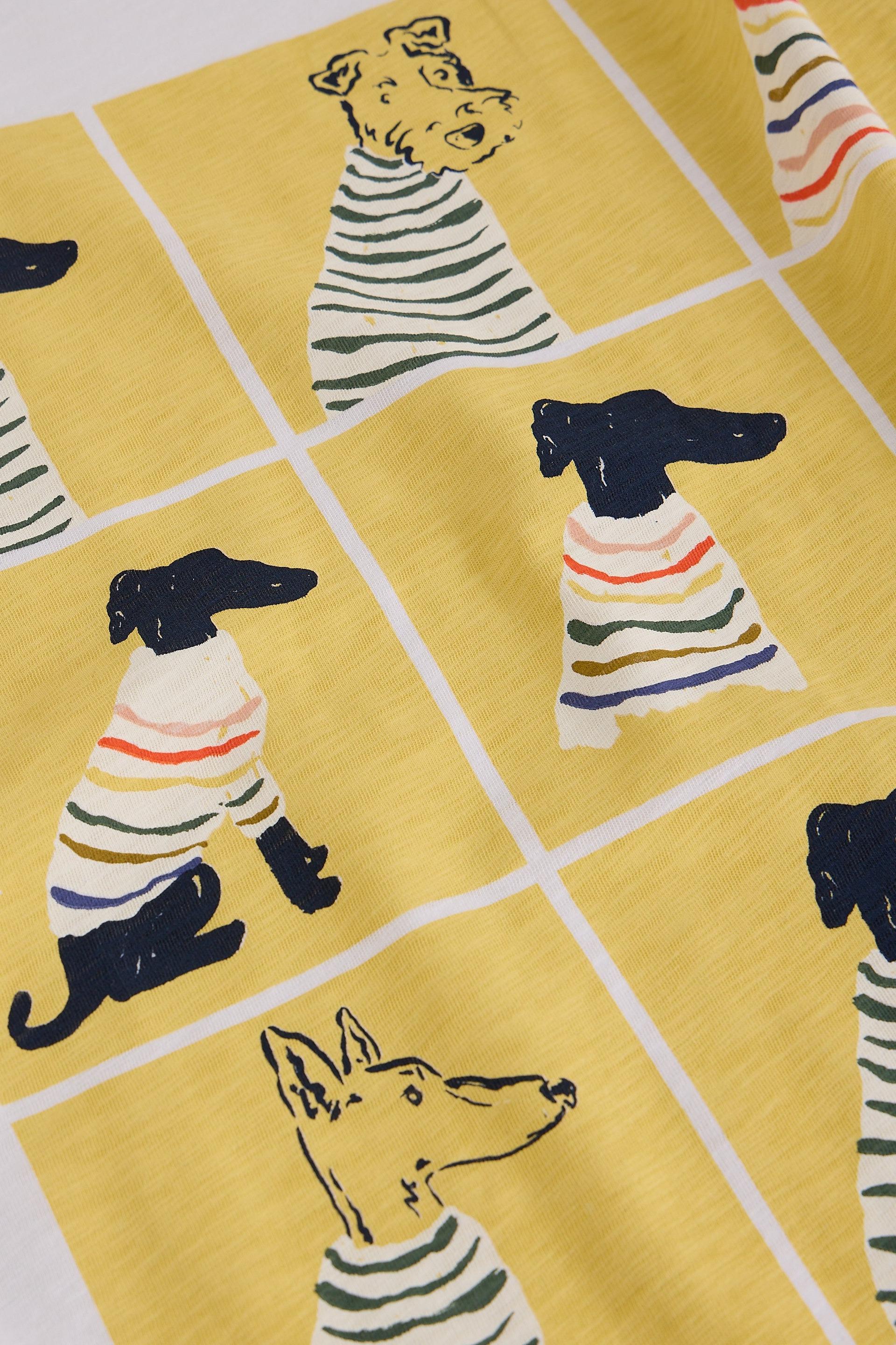 A close-up of a yellow fabric featuring cartoon dachshunds wearing striped sweaters, separated by white grid lines.